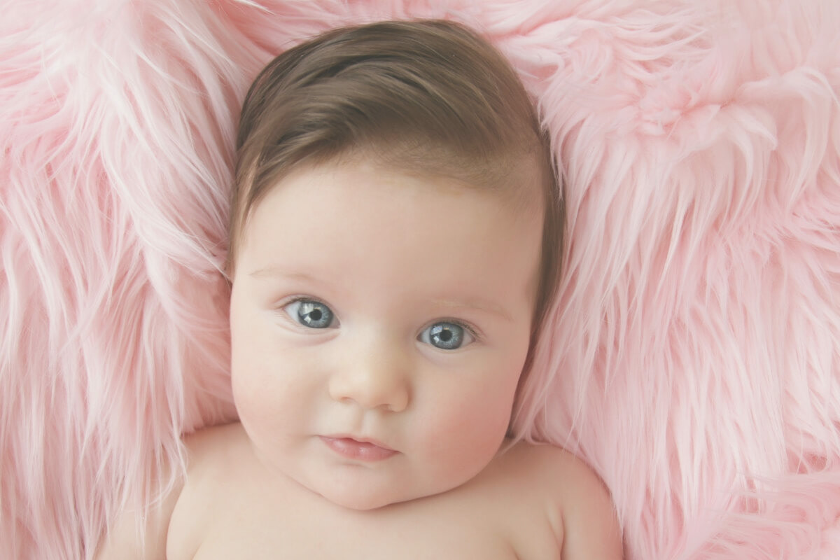 Photo of a baby looking at camera resting on a pink fluffy blanket