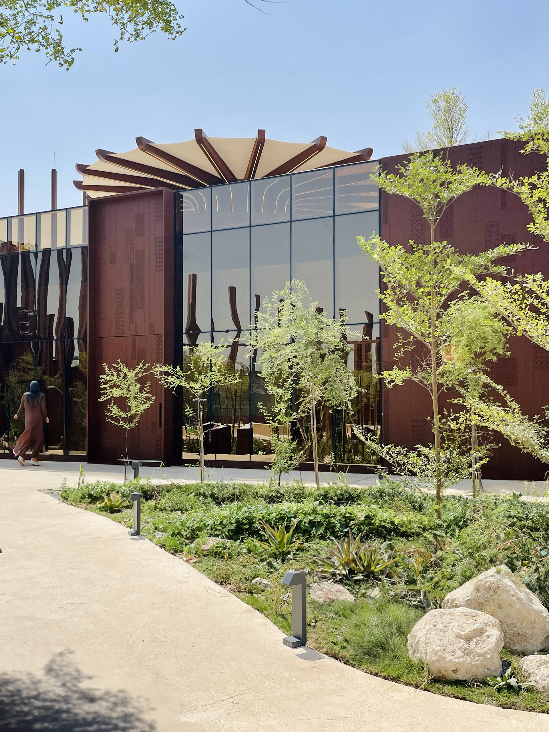 Internal lush garden with various species of Saudi Arabian plants and a wide sunshade covering the terrace in the background atop the main building