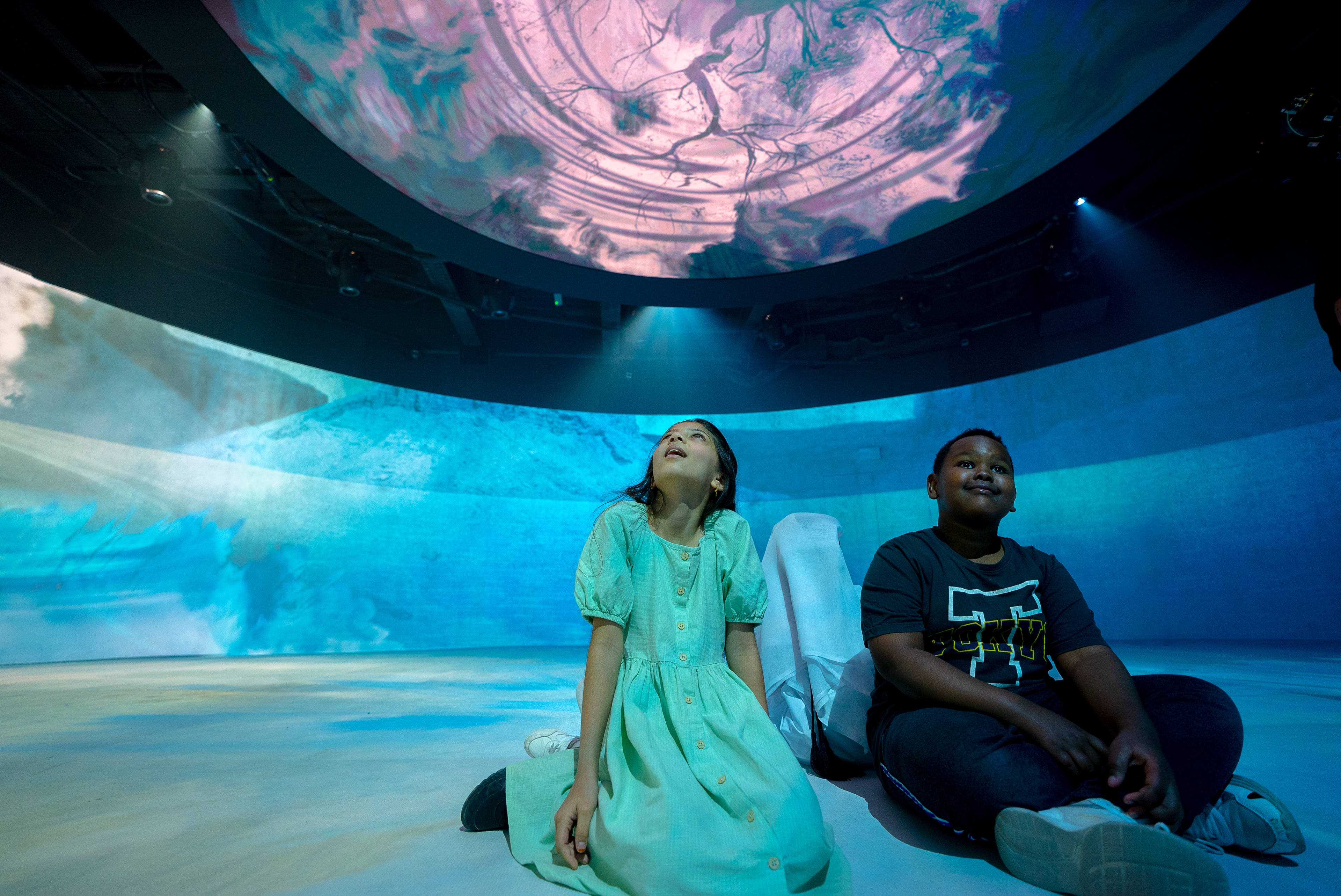 Children seated in the middle of the 360° theatre with a blue and waving light show