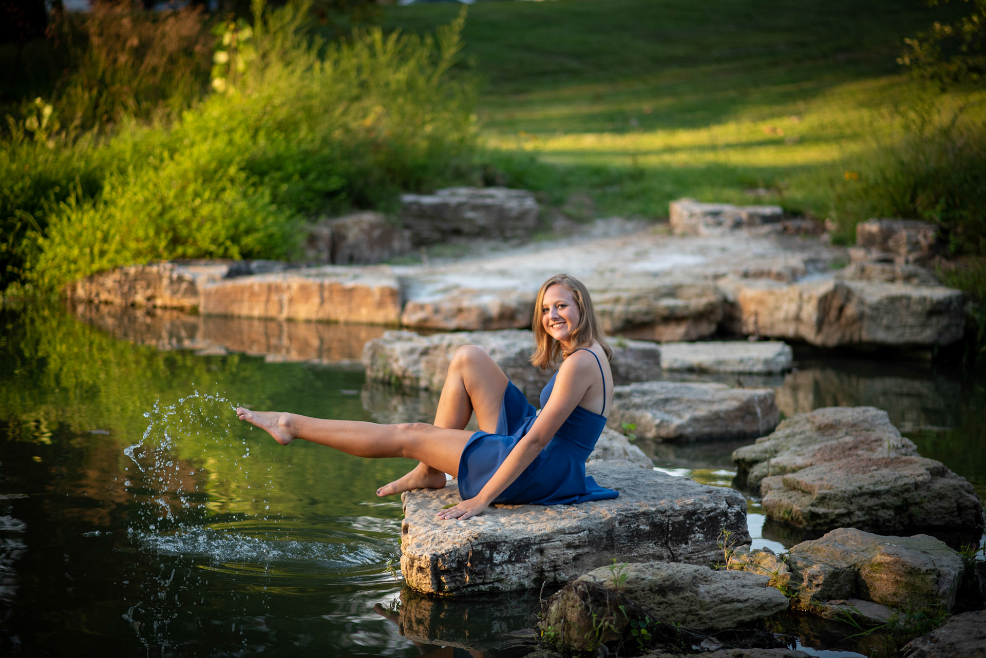 high school senior girl in a park kicking water in a blue dress