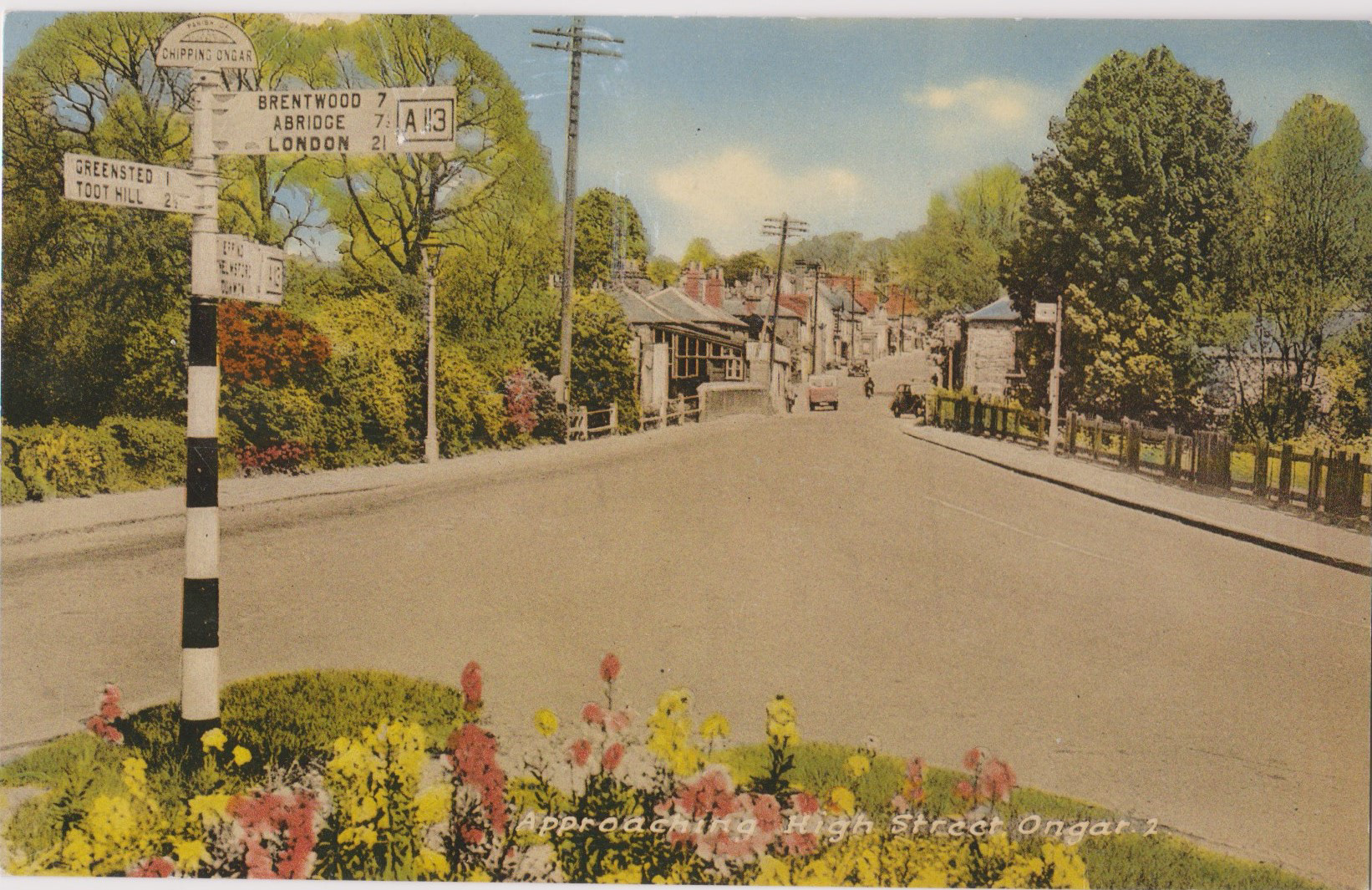 Approaching High Street Ongar, a hand-coloured postcard from the M and L National Series circa 1930