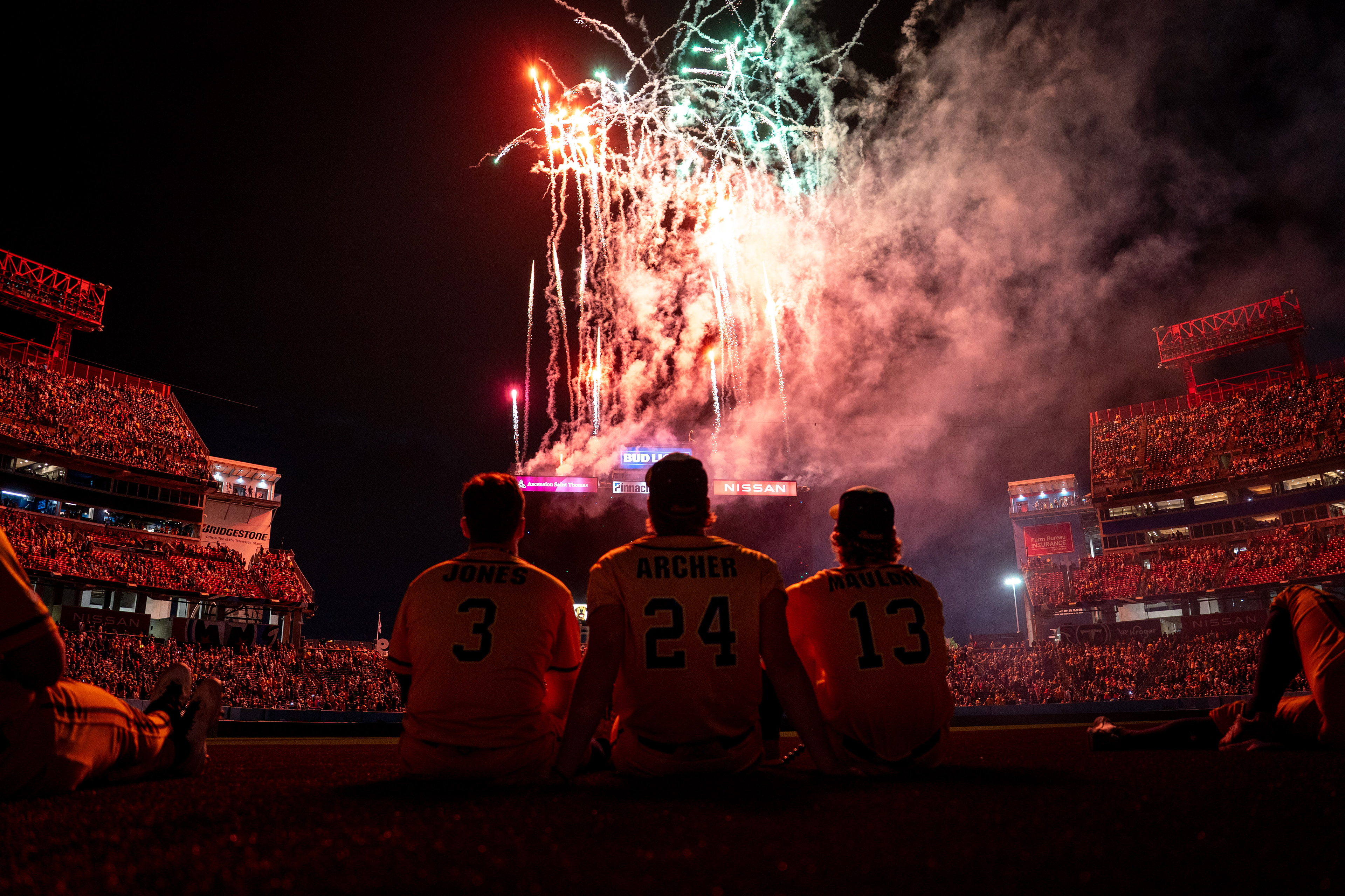 Savannah Bananas Eric Jones (3), left, Savannah Bananas Andy Archer (24), center, and Savannah Bananas Dalton Mauldin (13), right, watch as fireworks illuminate the sky after their game against the Party Animals at Nissan Stadium in Nashville, Tenn., Saturday, May 10, 2025.