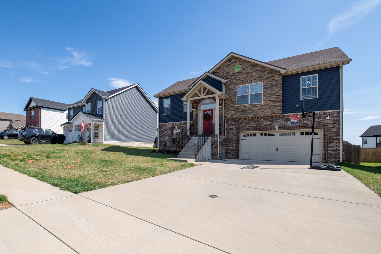Front exterior view of a two-story suburban home with brick and blue siding, a double garage, and a covered front porch—neighboring house visible to the right, all under a clear blue sky. Captured with clean lines and natural daylight to highlight curb appeal and residential charm.