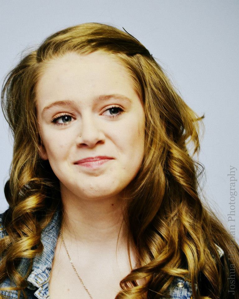 “Senior portrait of a girl with light brown curly hair worn down, subject in a denim jacket over a white top, posed in front of a light neutral backdrop—clean, confident, and timeless.