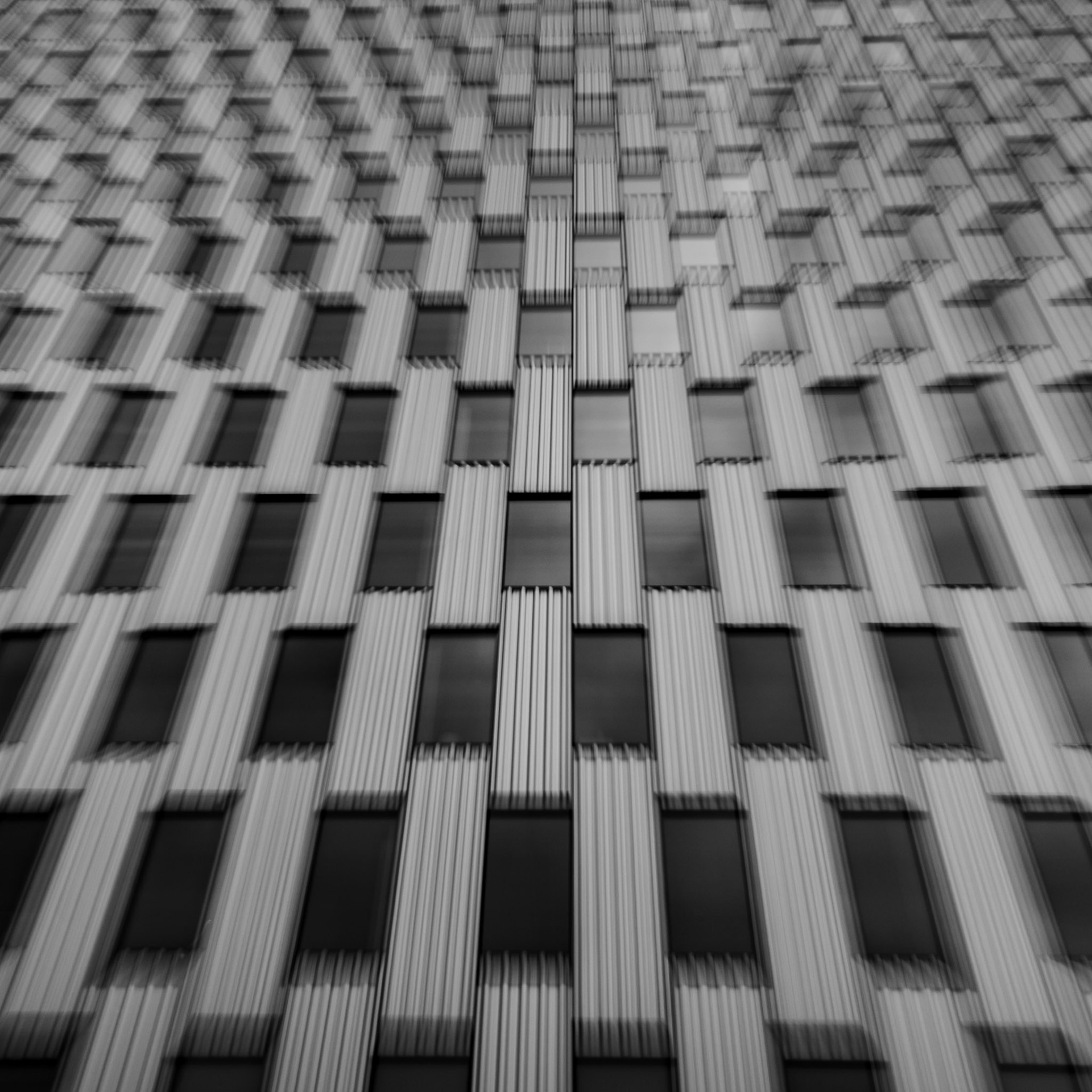 Abstract black and white architectural facade featuring a repeating grid of windows viewed from below.