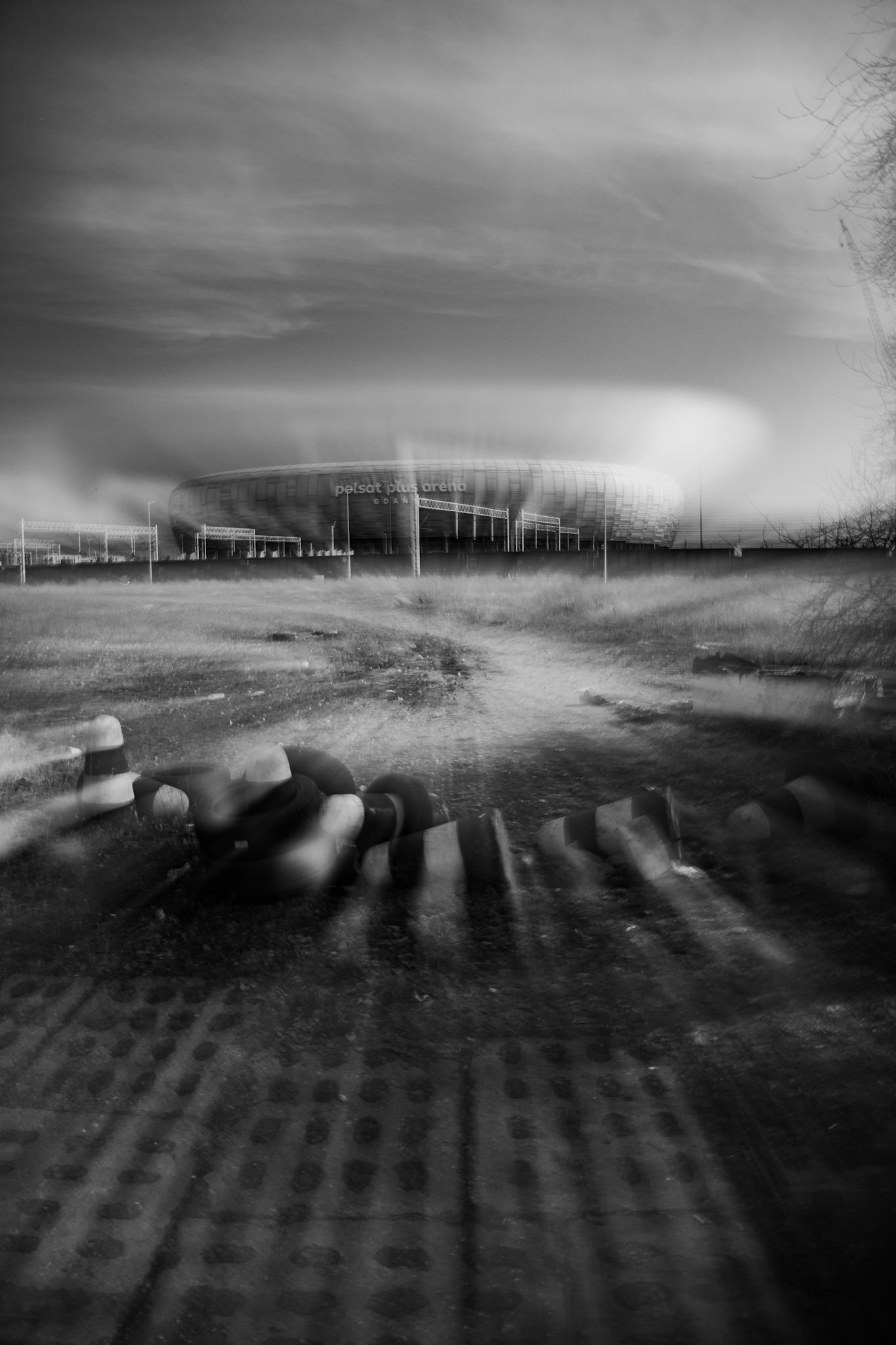 Black and white long-exposure photo of a stadium with motion blur in the foreground and dramatic cloudy sky.