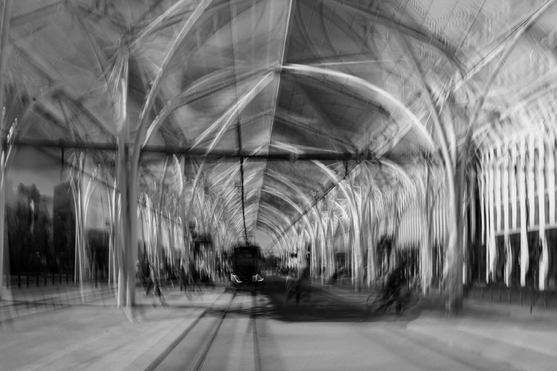 Modern tram station with arched steel and glass canopy, black and white urban architecture photo in ICM technique.