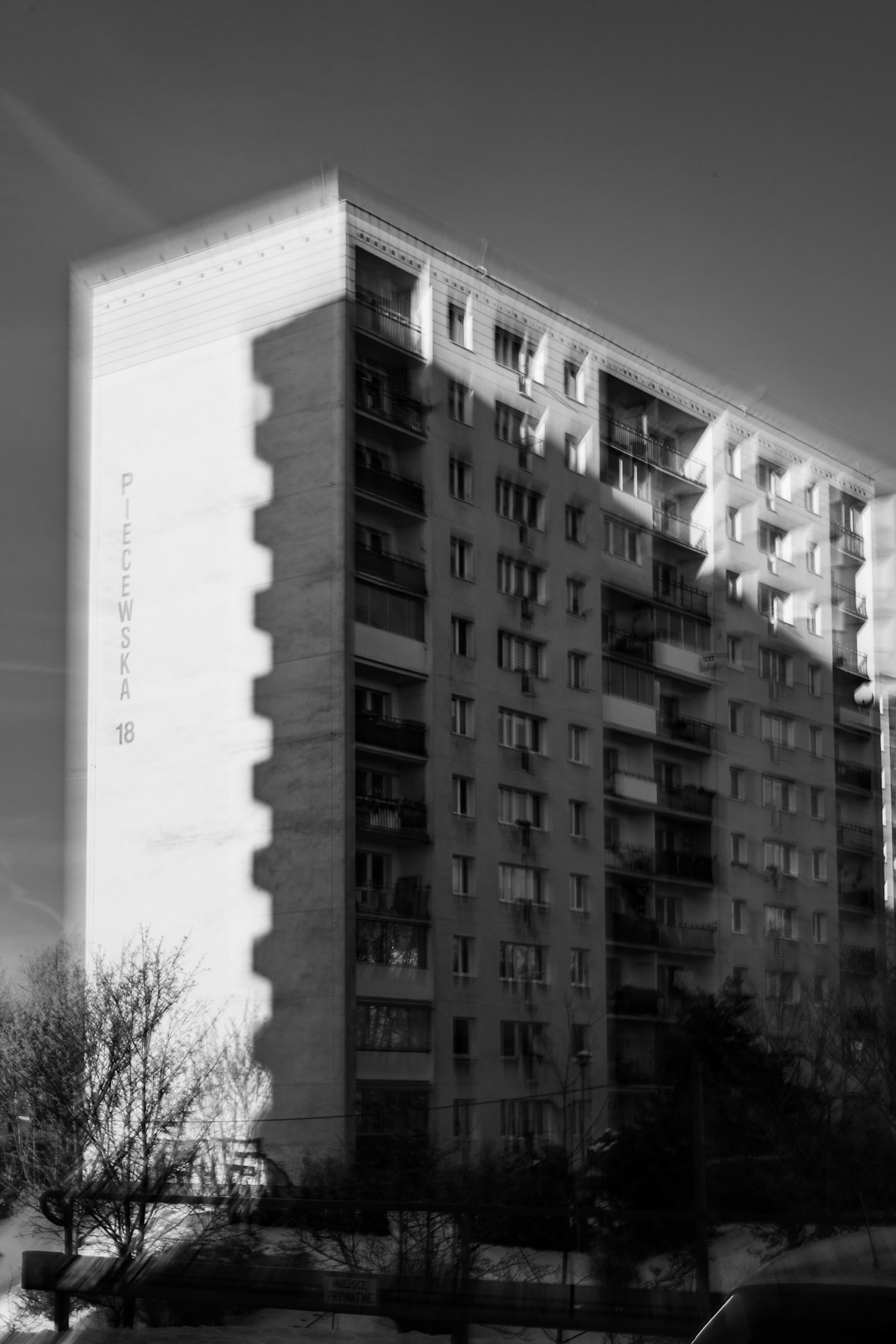 Black and white photograph of a mid-century apartment building with balconies, motion blur effect, urban residential architecture.