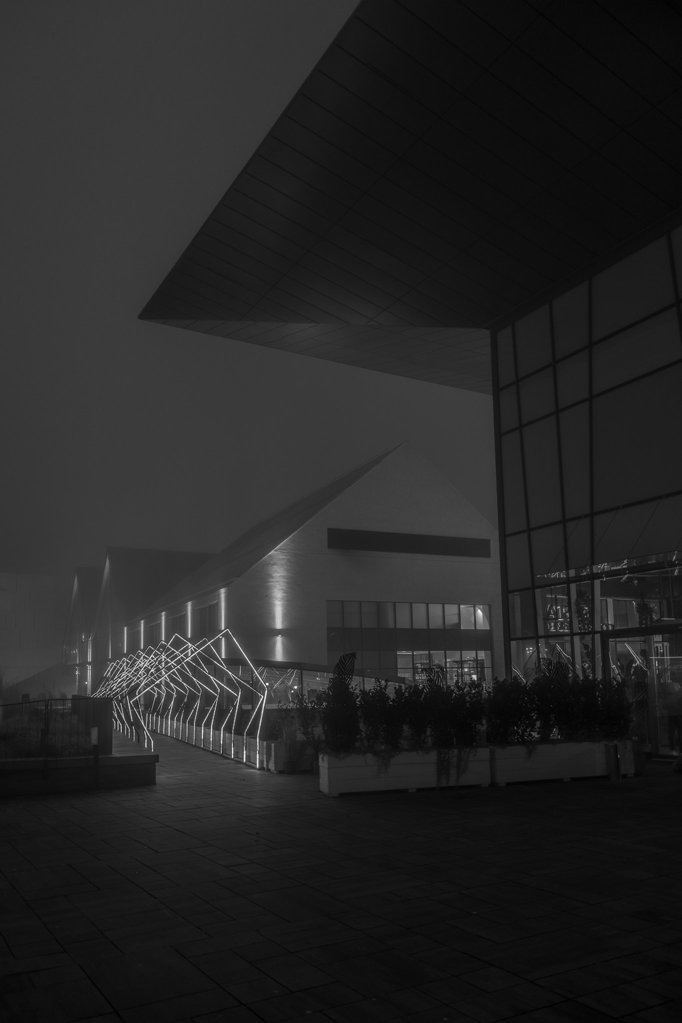 Modern architectural building at night with illuminated geometric walkway and foggy atmosphere, showcasing contemporary design and dramatic lighting.