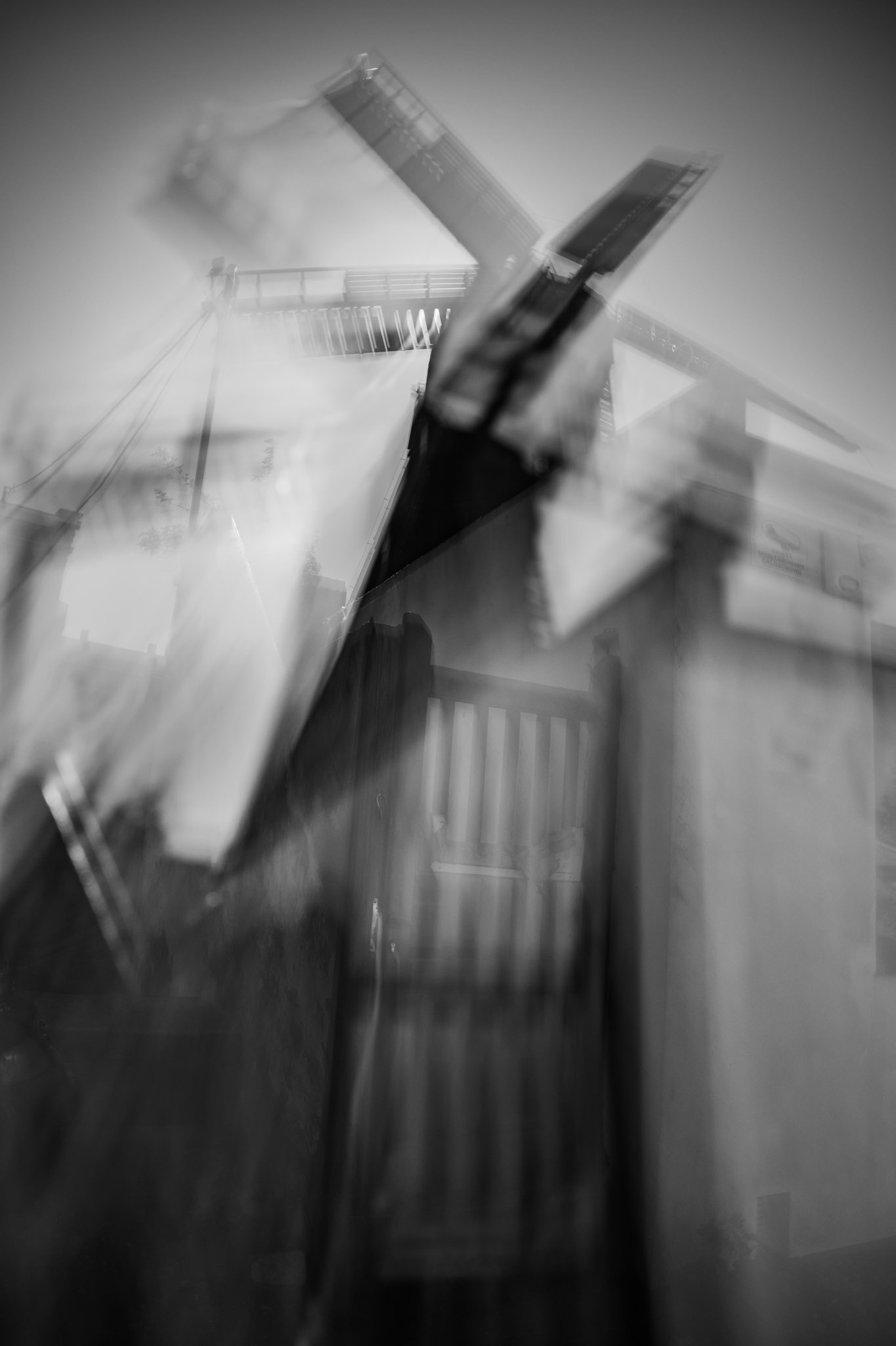 Blurred black-and-white image of a traditional windmill captured with motion blur and abstract camera movement, creating a dreamy, ghostlike effect.