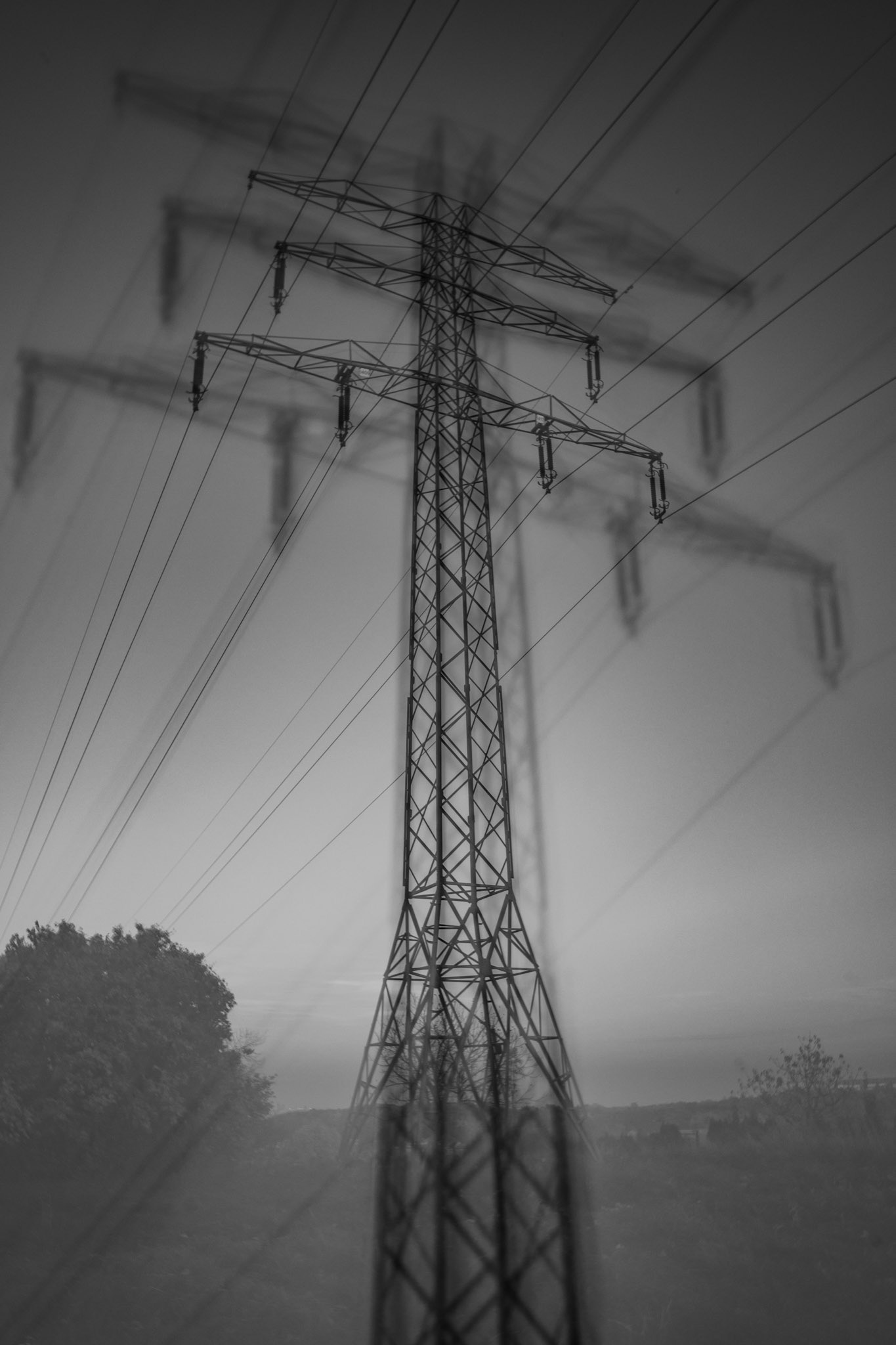 Black and white ICM photography of a power transmission tower with blurred motion effects and power lines stretching into the sky, creating an abstract industrial landscape.