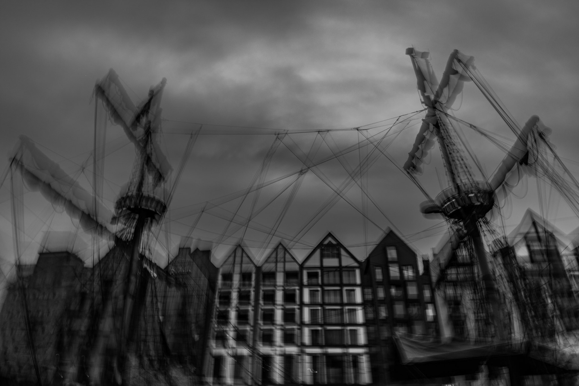 Black-and-white long-exposure photograph of industrial harbor cranes and waterfront buildings beneath a dramatic cloudy sky.