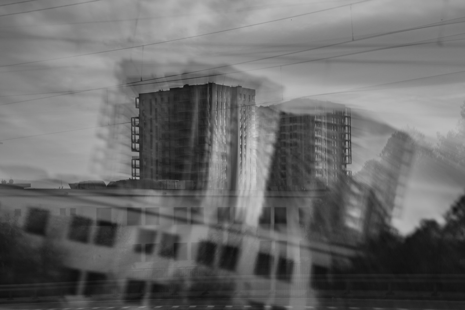Abstract black and white ICM photography of urban buildings with motion blur effect, featuring tall residential towers and modern architecture under a cloudy sky.