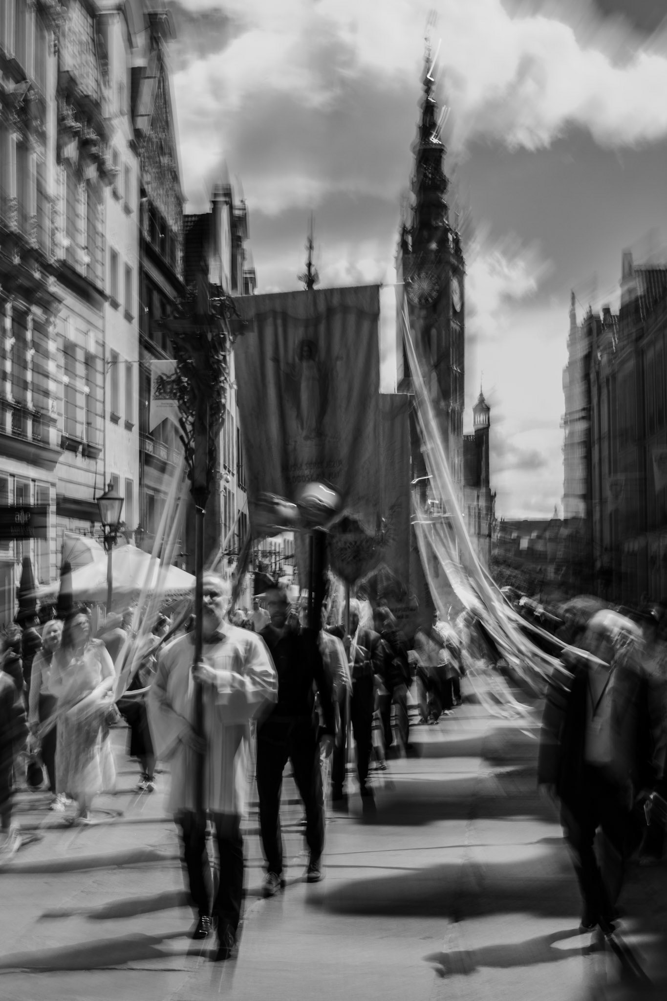Black-and-white religious procession in a historic European city with banners, crowds, and artistic motion blur.