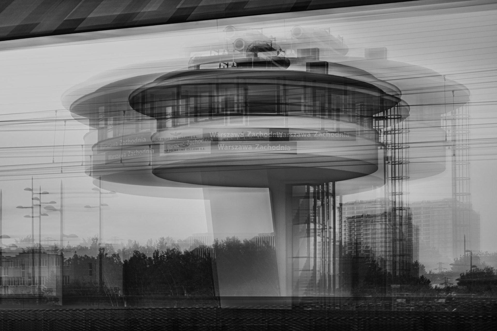 Black-and-white long exposure photograph of the iconic circular Warszawa Zachodnia railway station in Warsaw, Poland, with intentional motion blur creating a dynamic, abstract architectural effect.