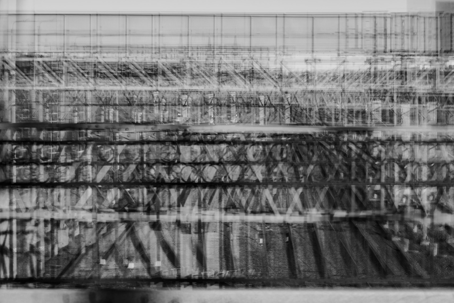 Black-and-white abstract image of layered steel bridge structures, with multiple overlapping exposures creating a blurred, geometric pattern of beams and trusses.