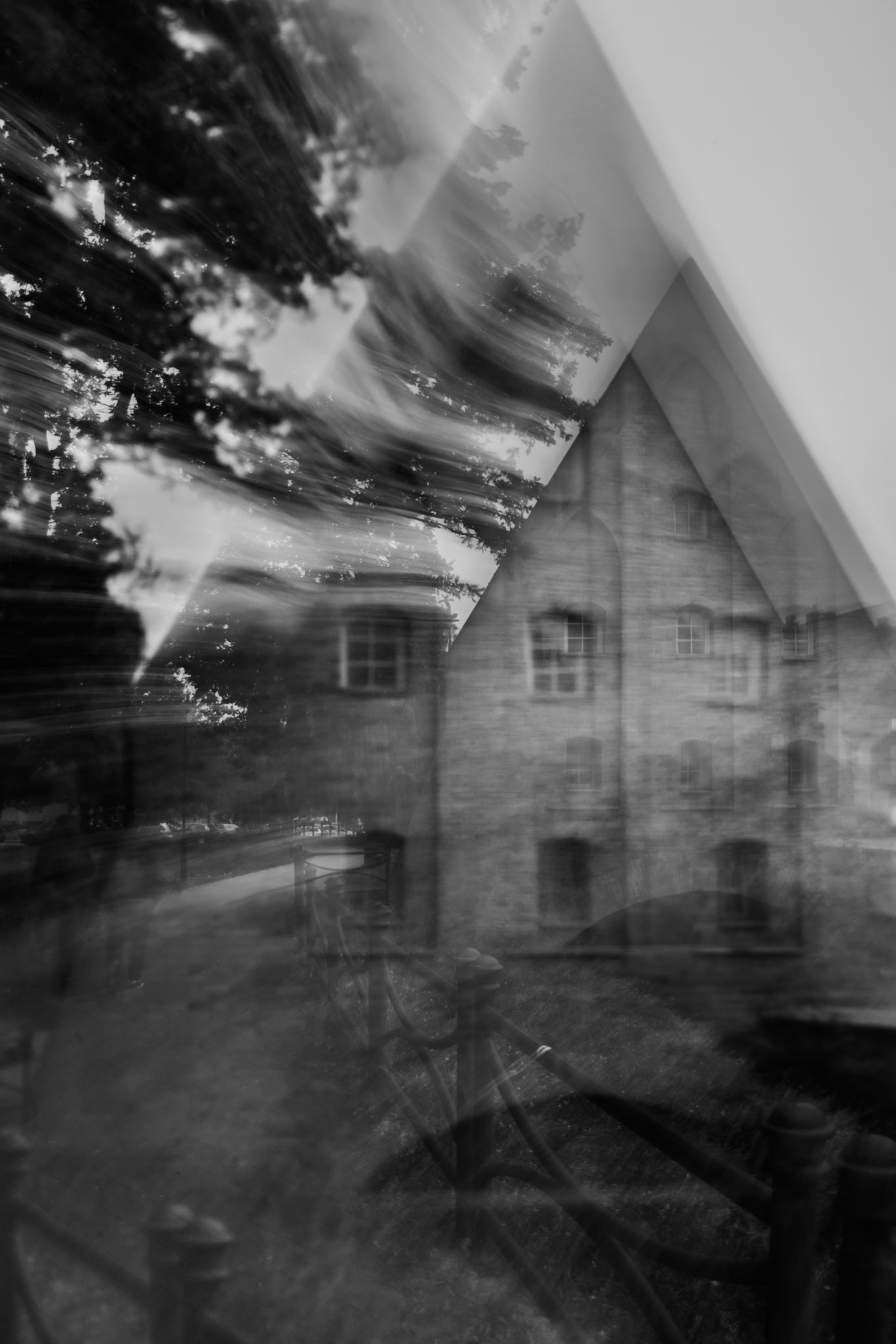 Black and white artistic photo of an old brick building with a steep gable roof, captured with long exposure and ICM technique showing blurred motion of trees and light.