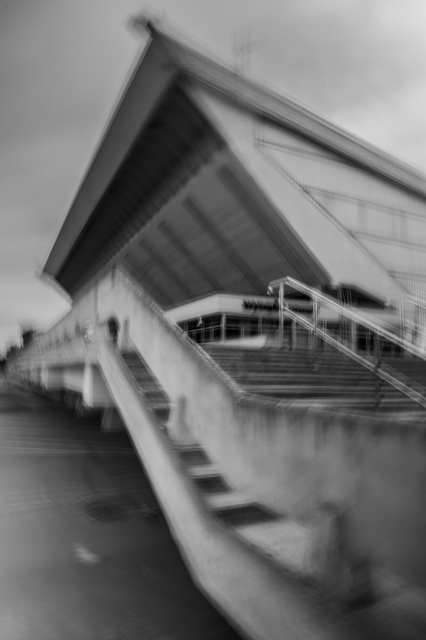 Modern concrete building with large roof and staircase, black and white architectural photo in ICM technique.