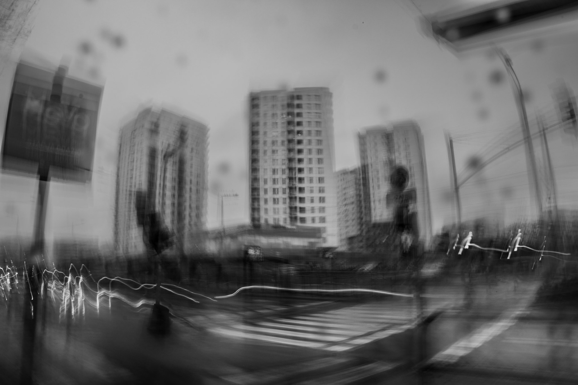 Blurred, black and white ICM photograph of a city scene, taken under low-light conditions, conveying a sense of movement and urban atmosphere.
