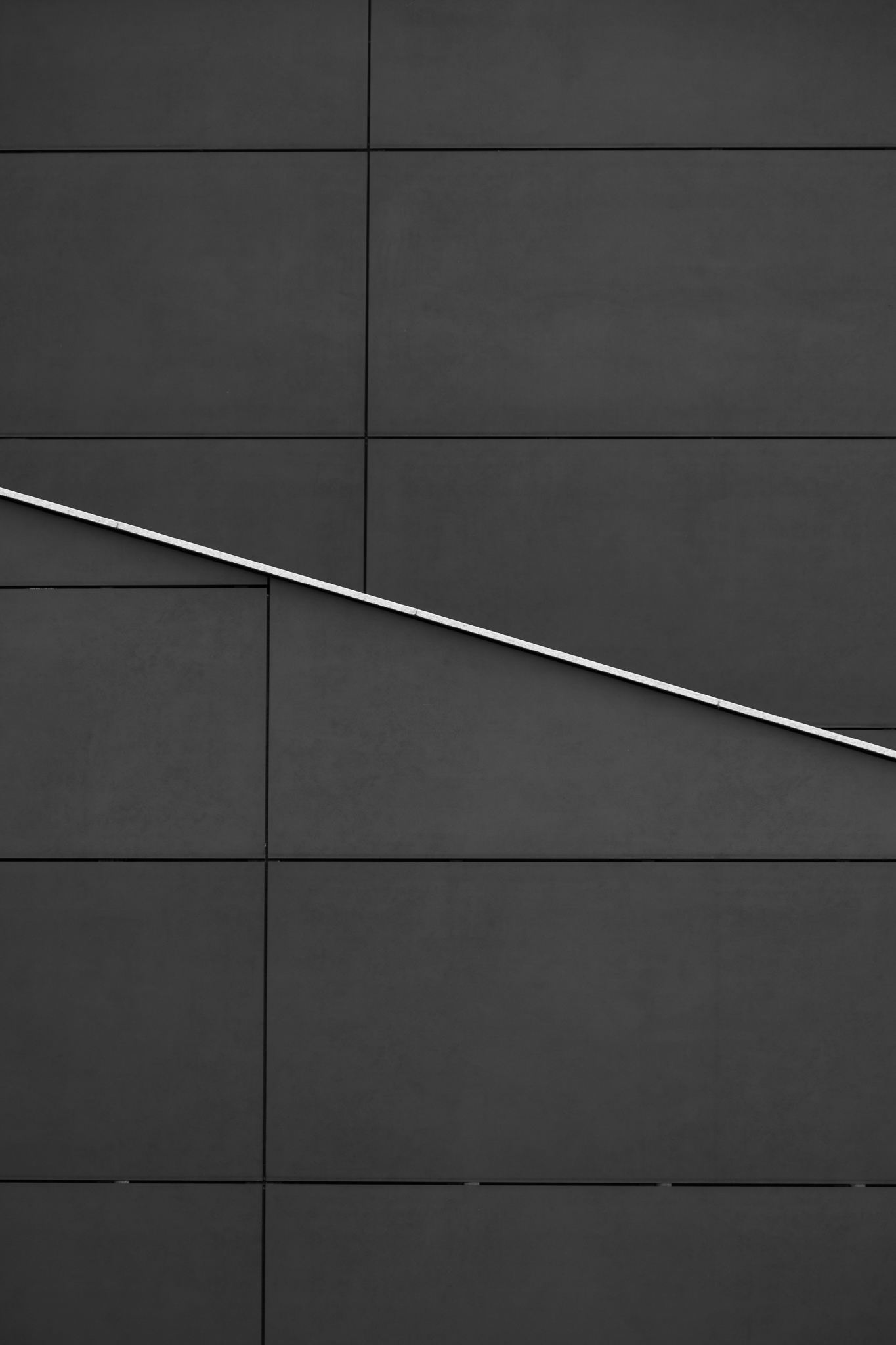 Minimalist dark gray tiled wall with diagonal metal handrail, modern geometric architectural background.