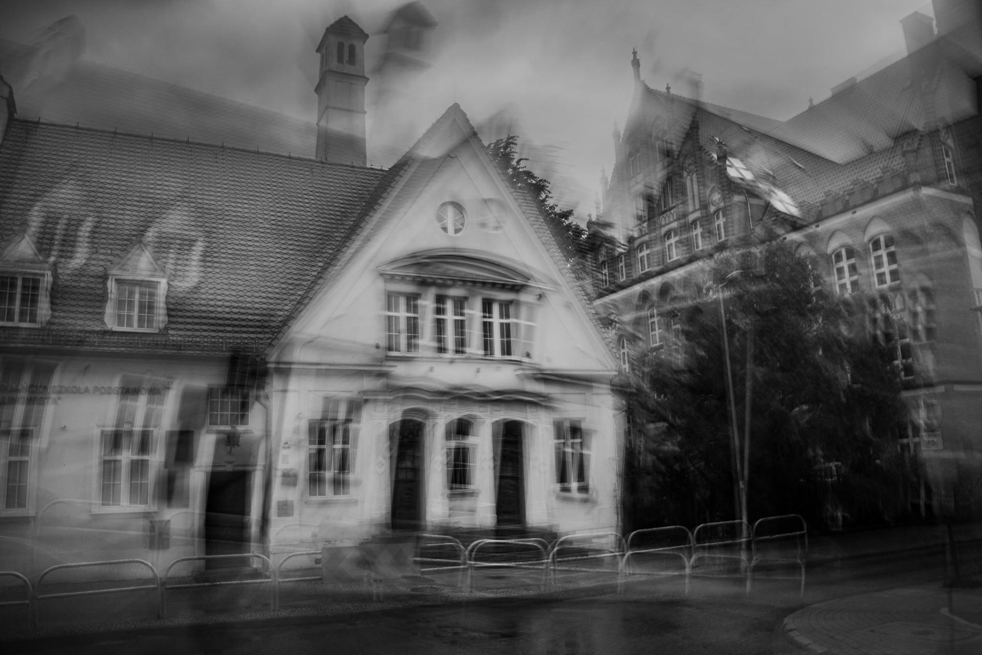 Black-and-white motion-blur photograph of historic European-style buildings on a rainy street, creating a ghostly, dreamlike urban scene.