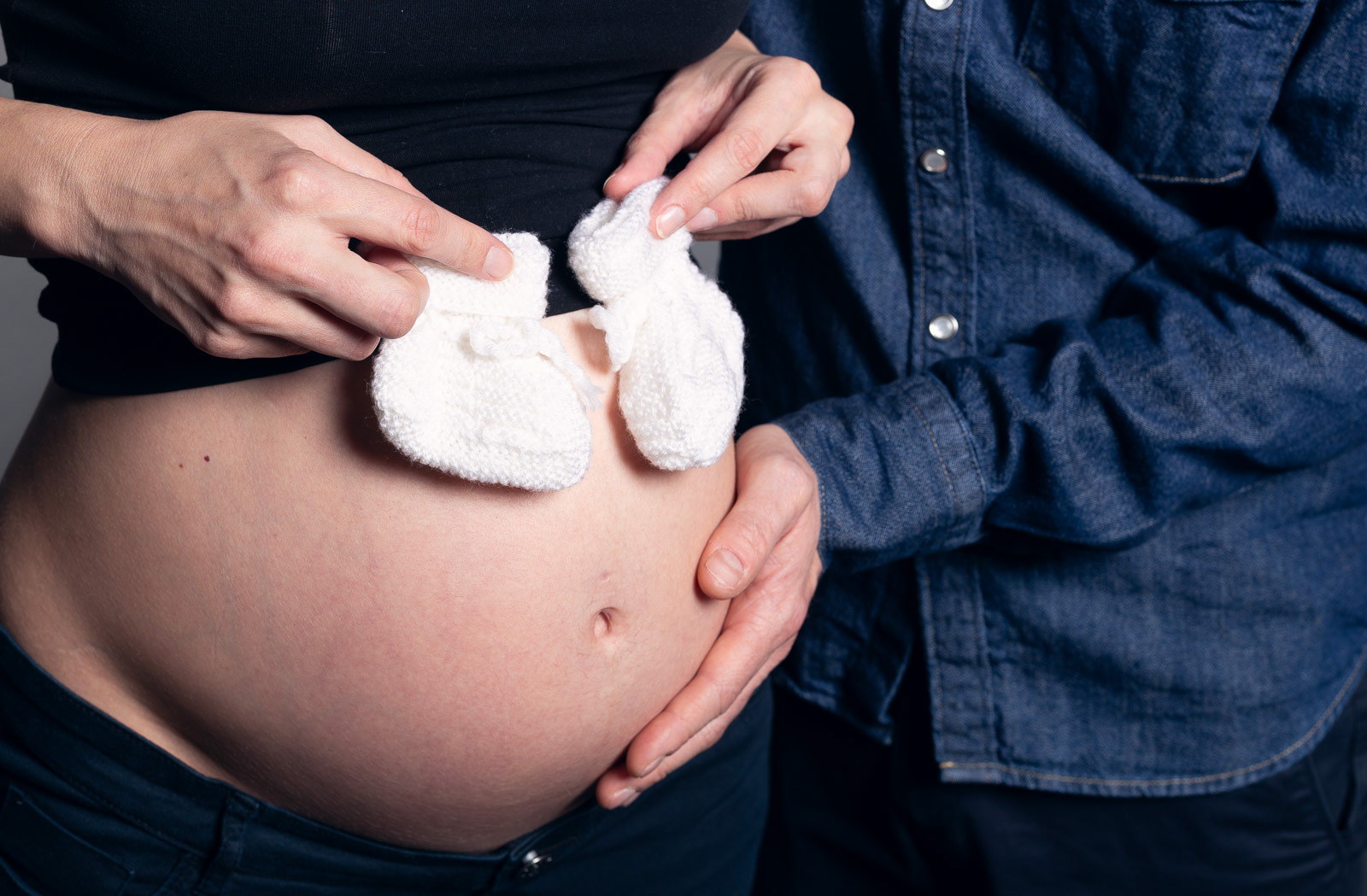 Photo de grossesse - à Lyon - naturelle et lumineuse - ventre de maman avec main de papa et chaussons du bébé à venir
