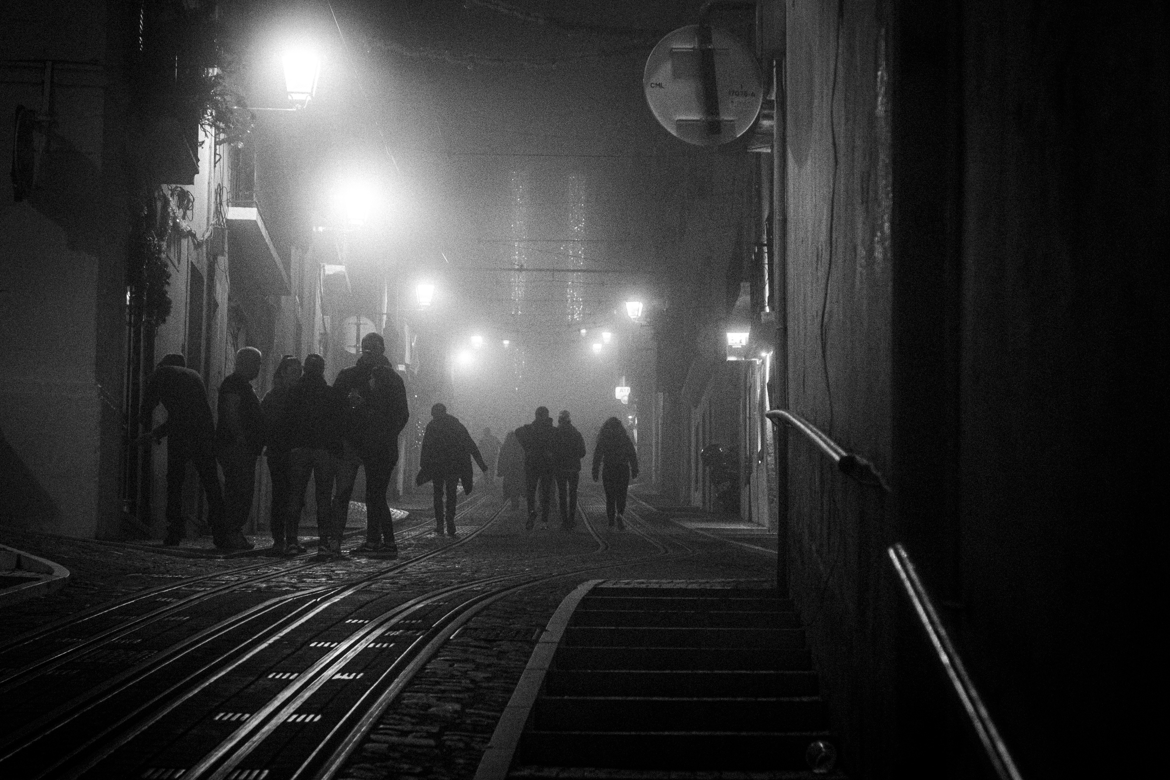 Groups of people are seen against a foggy background in this black and white night scene in central Lisbon