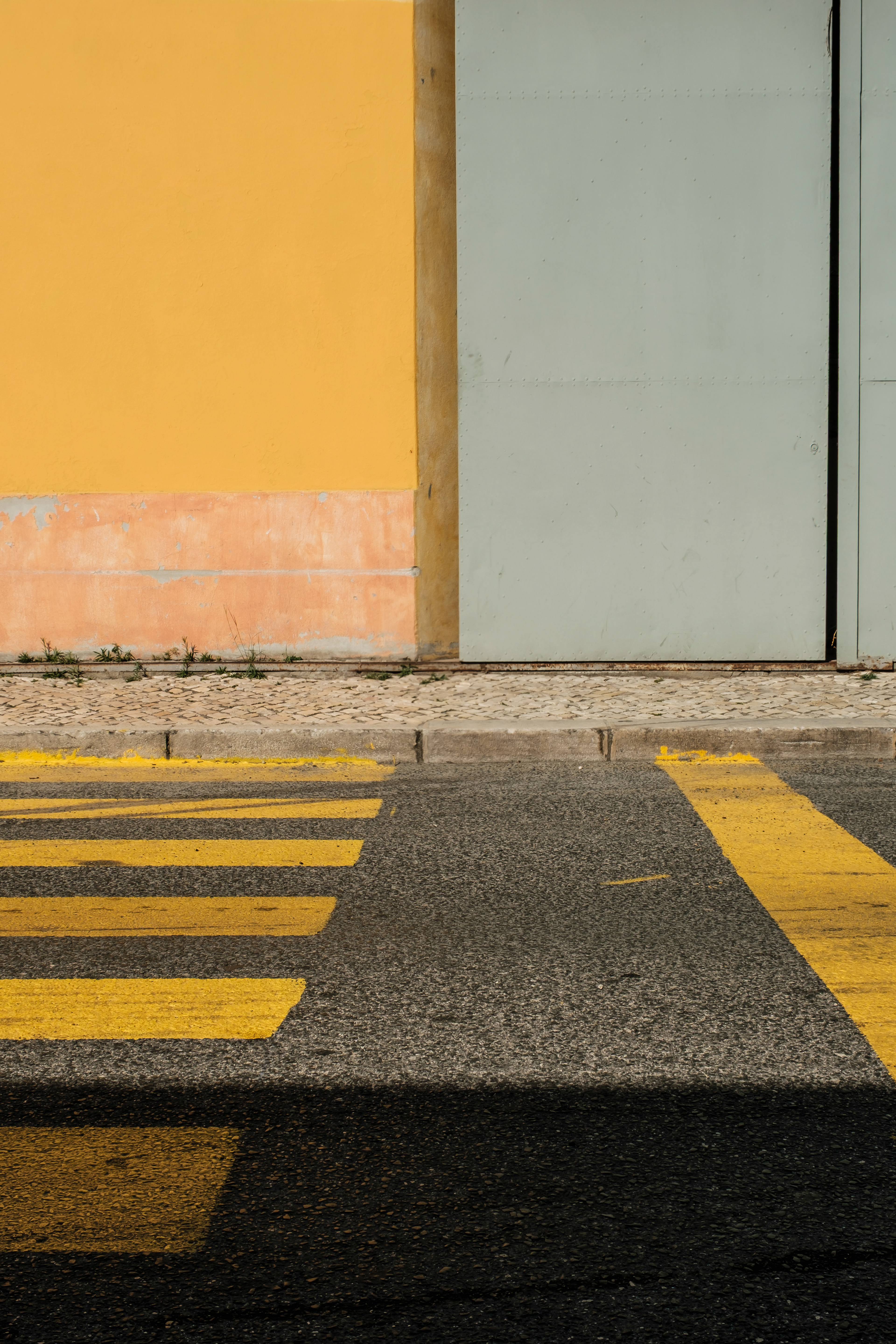 a yellow pedestrian crossing leading to a grey warehouse door and yellow wall