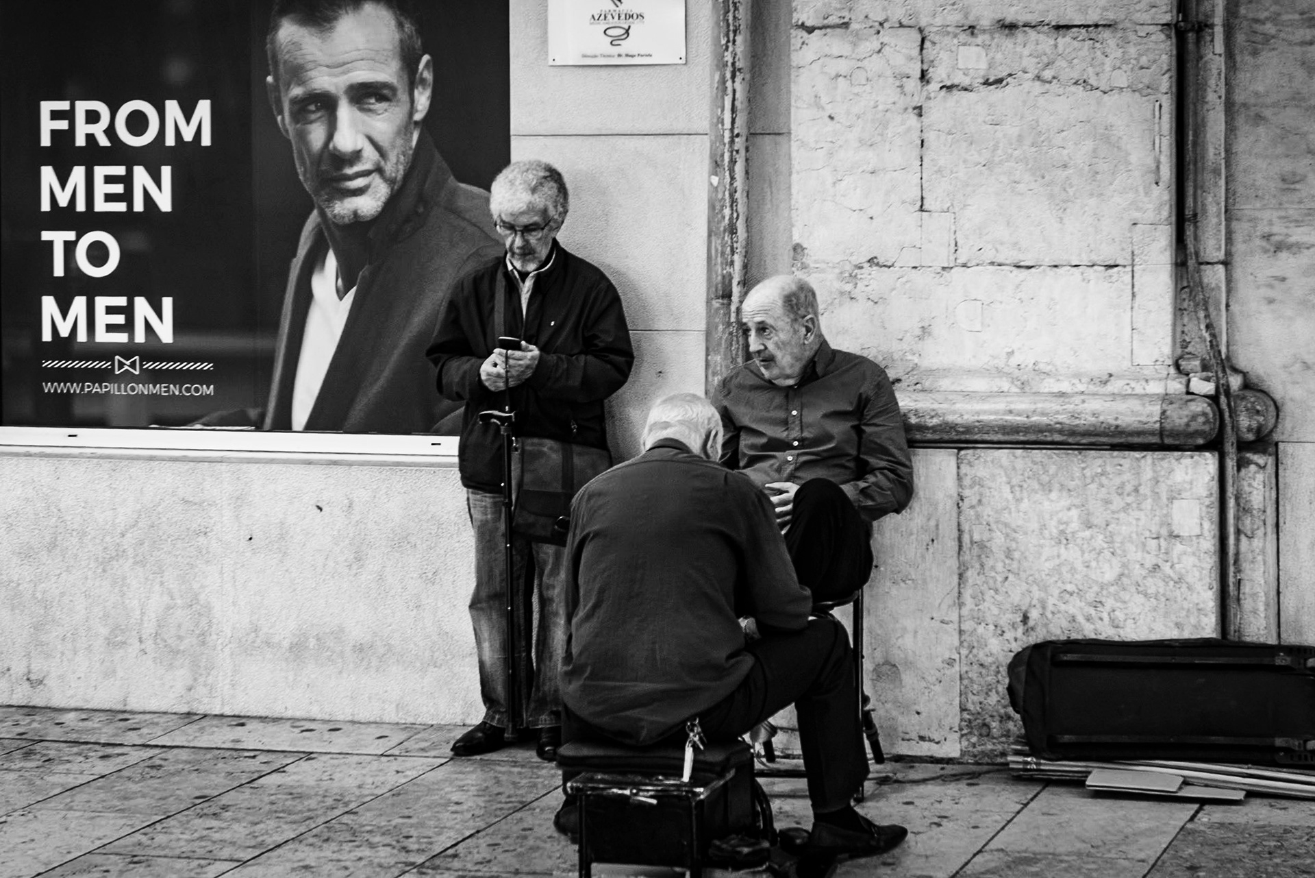 Black and white image with three men in front of an ad that reads 'from men to men"