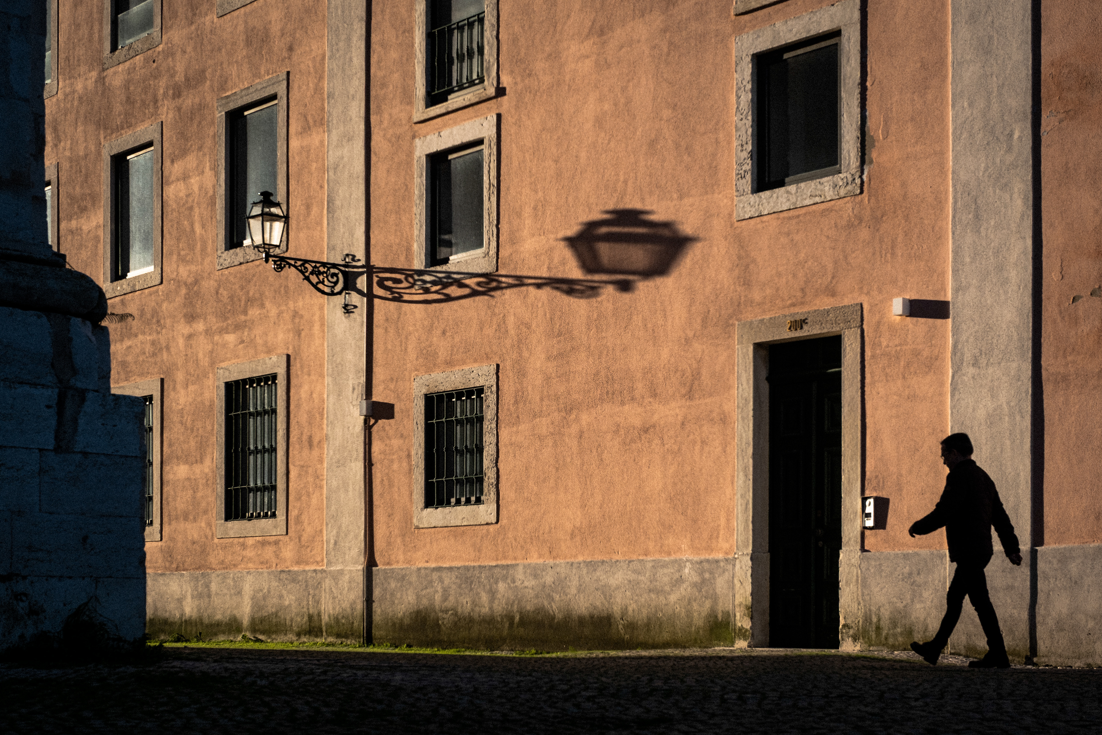 The silhouette of a man who walks in front of a salmon-painted house in Lisbon