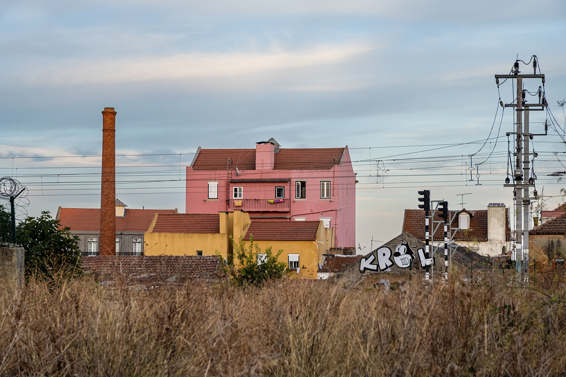 A pink-painted house and a factory chimney behind a vacant lot in central Lisbon