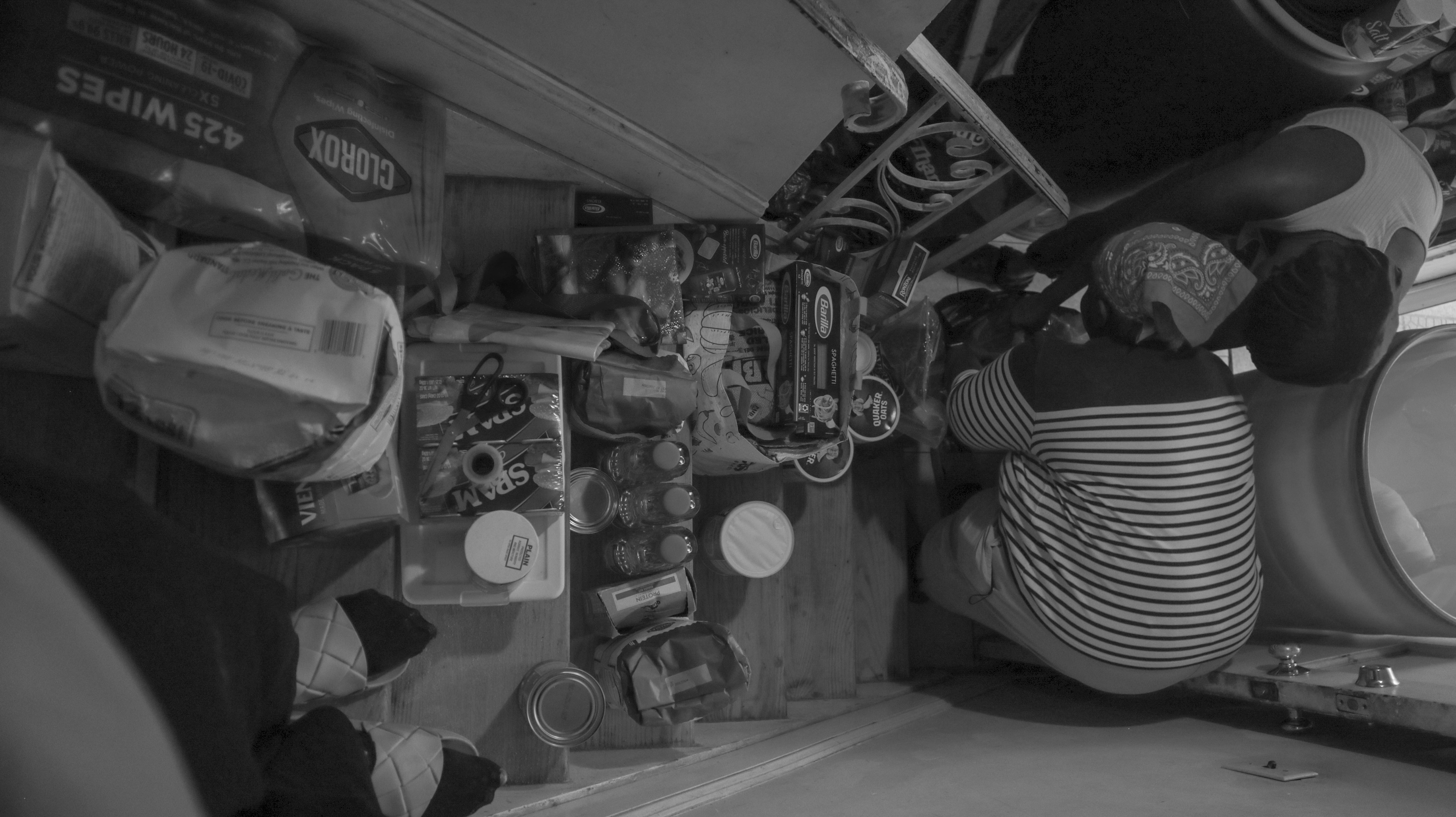 Myrtho and her niece, Cassandra, take out items from shopping bags. Myrtho has all of the items stacked on a staircase. Cassandra has her own collection of goods that will also go to her mother, Esther.
