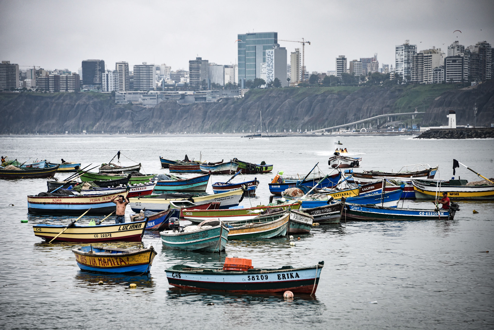 Lima, Peru - Nov 17, 2019: Fishing boats in Chorrilos harbour against the backdrop of the commerical Miraflores district