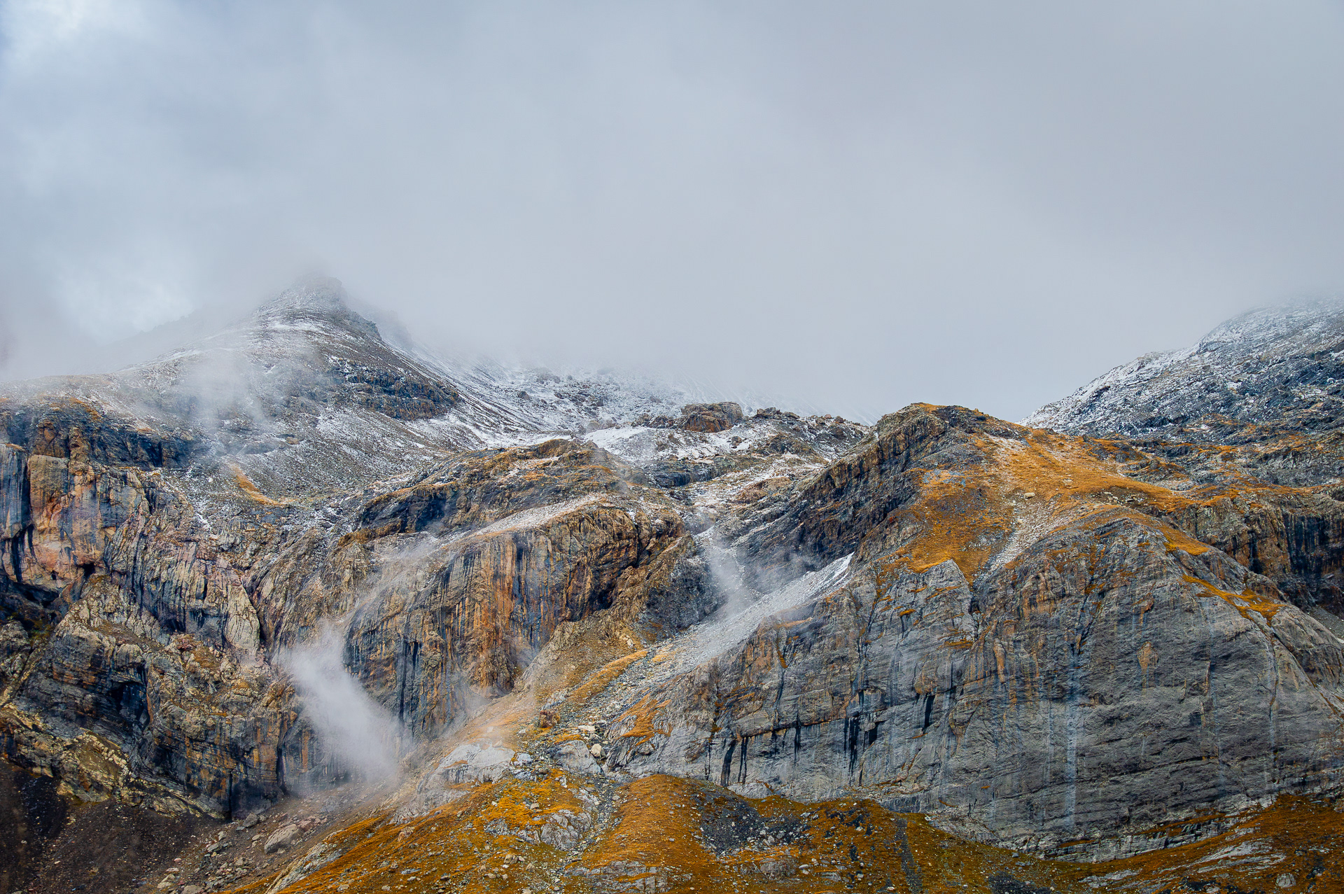 Mountains in the Clouds’: From the Alpine Moods series, rugged rock faces and golden tundra peaks weaving through a thick blanket of low-hanging grey clouds and mist.