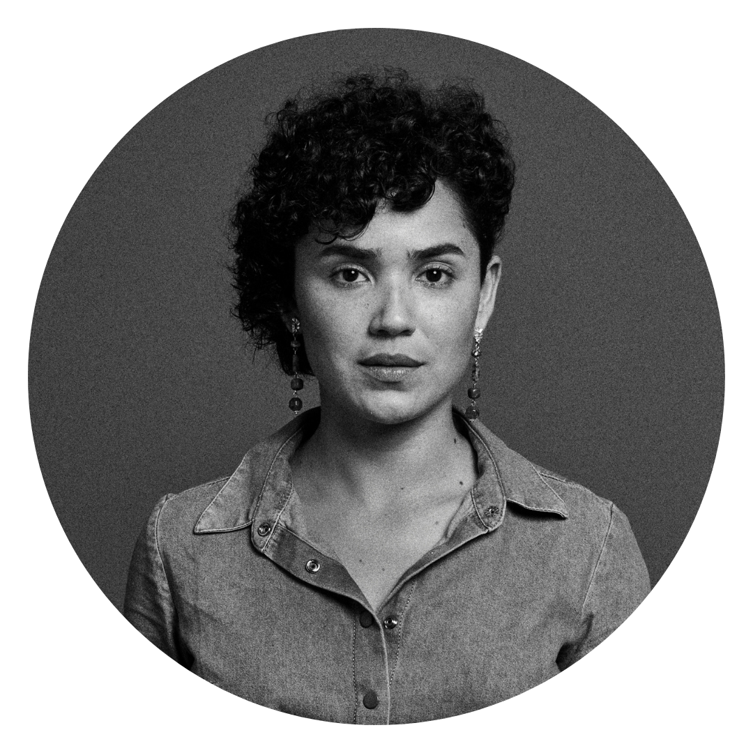 Black and White portrait of a black woman with short curly hair, wearing a jeans shirt. She is a Brooklyn-based visual storyteller specializing in music, dance, documentary, and portrait photography, capturing authentic moments with creativity and passion.