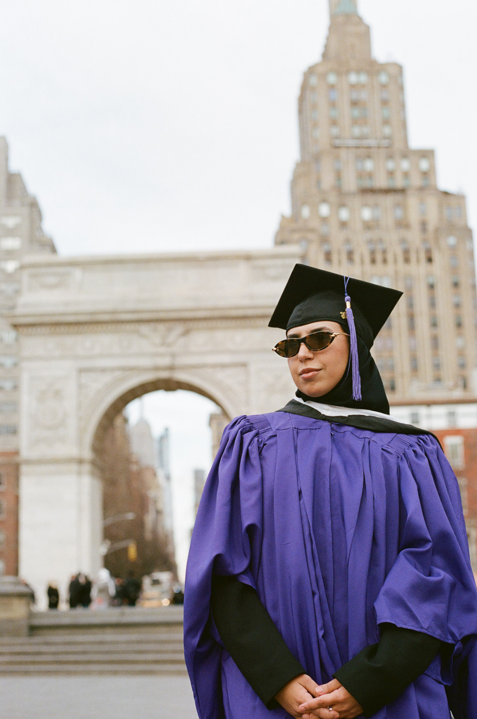 Muslim woman graduate in cap and gown standing near Washington Square Arch in NYC