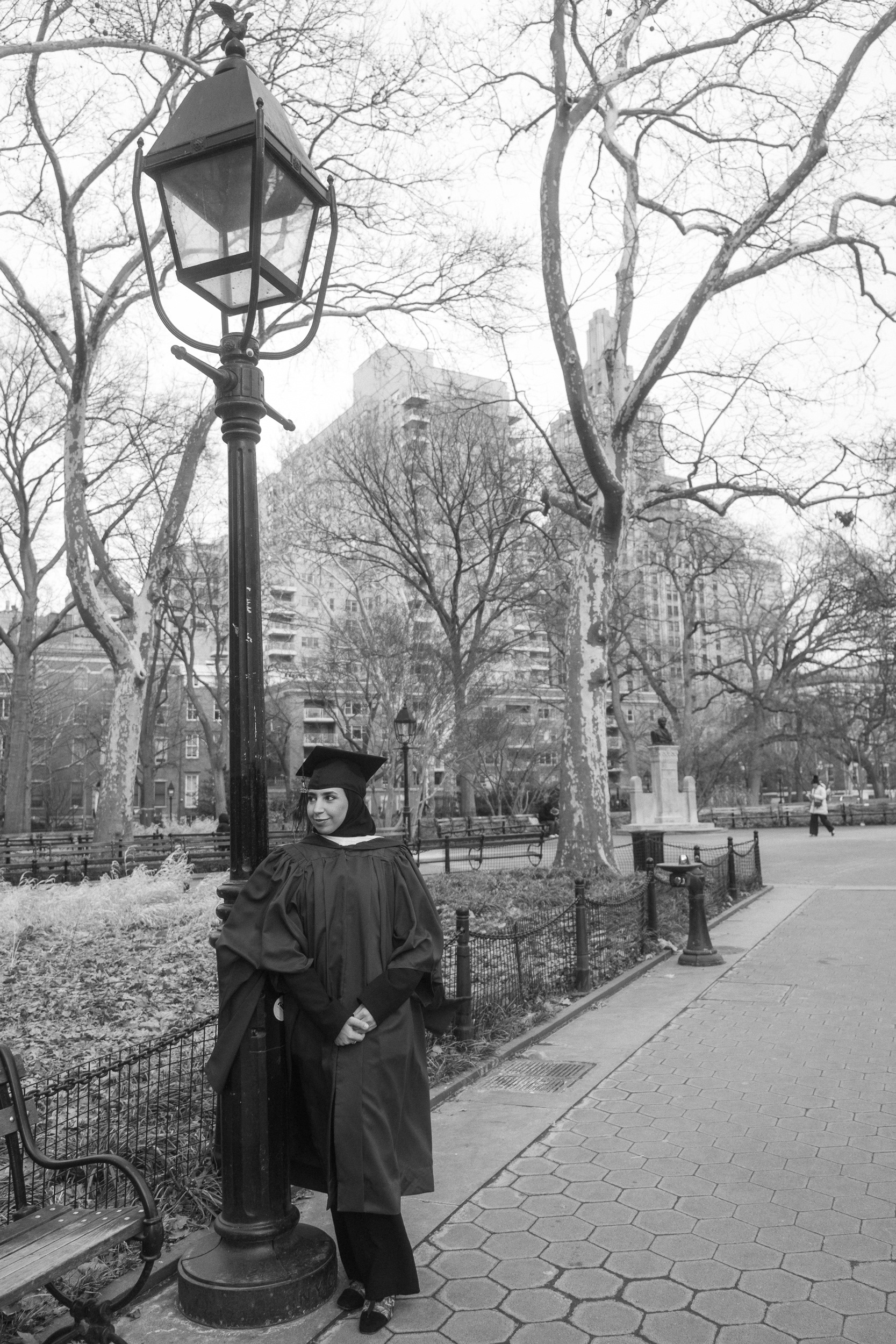 Graduate walking through Washington Square Park with city life in the background, NYC graduation photography