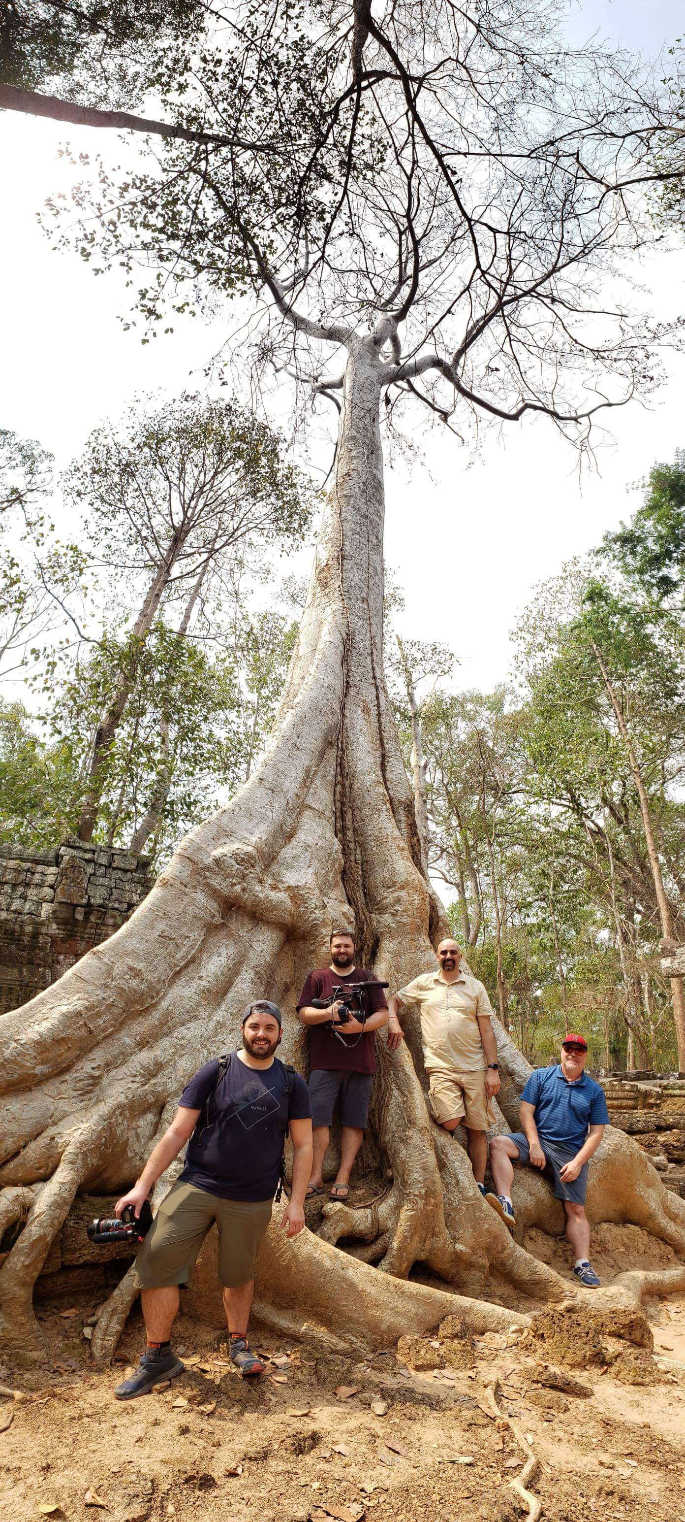 The Detours crew posing near one of the incredible features of Ta Prohm: massive trees and their roots overgrowing the ancient temple structures.