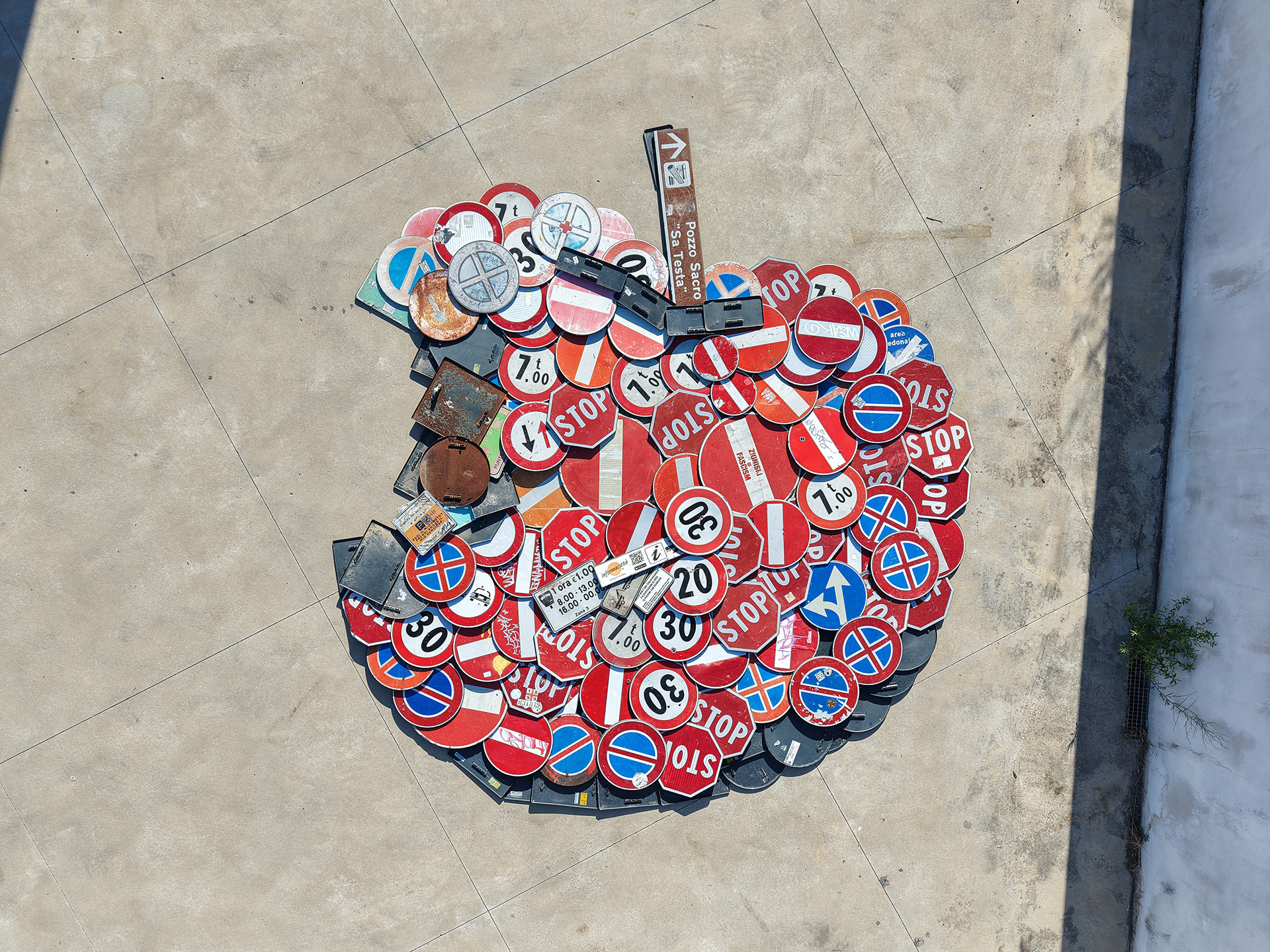 Aerial view of Concerto 0, a large apple assembled from discarded red, white and blue traffic signs on concrete.