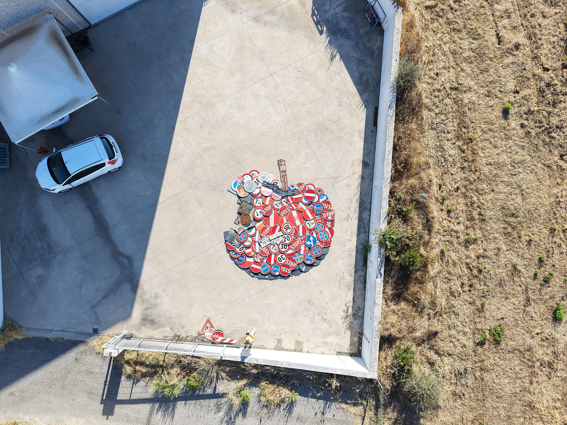 High aerial view of Concerto 0 beside a parked car, revealing the scale of the traffic-sign installation.