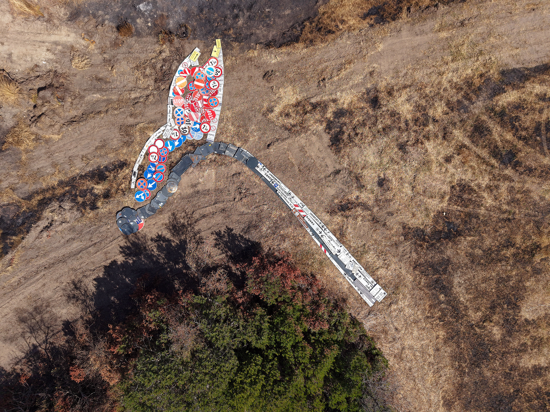 Close aerial view of a half-burnt match formed from intact reclaimed road signs, with red, white and blue faces creating the flame and grey metal backs forming the charred section.