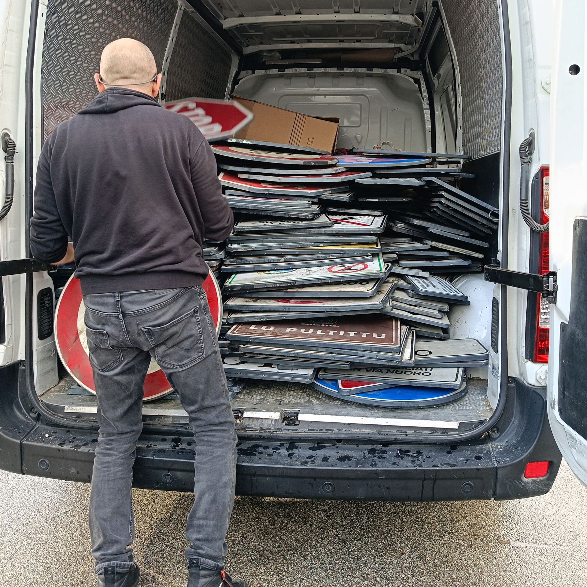 Scoobafish stands with his back to the camera before a van packed with discarded traffic signs collected for Urban Pixel.