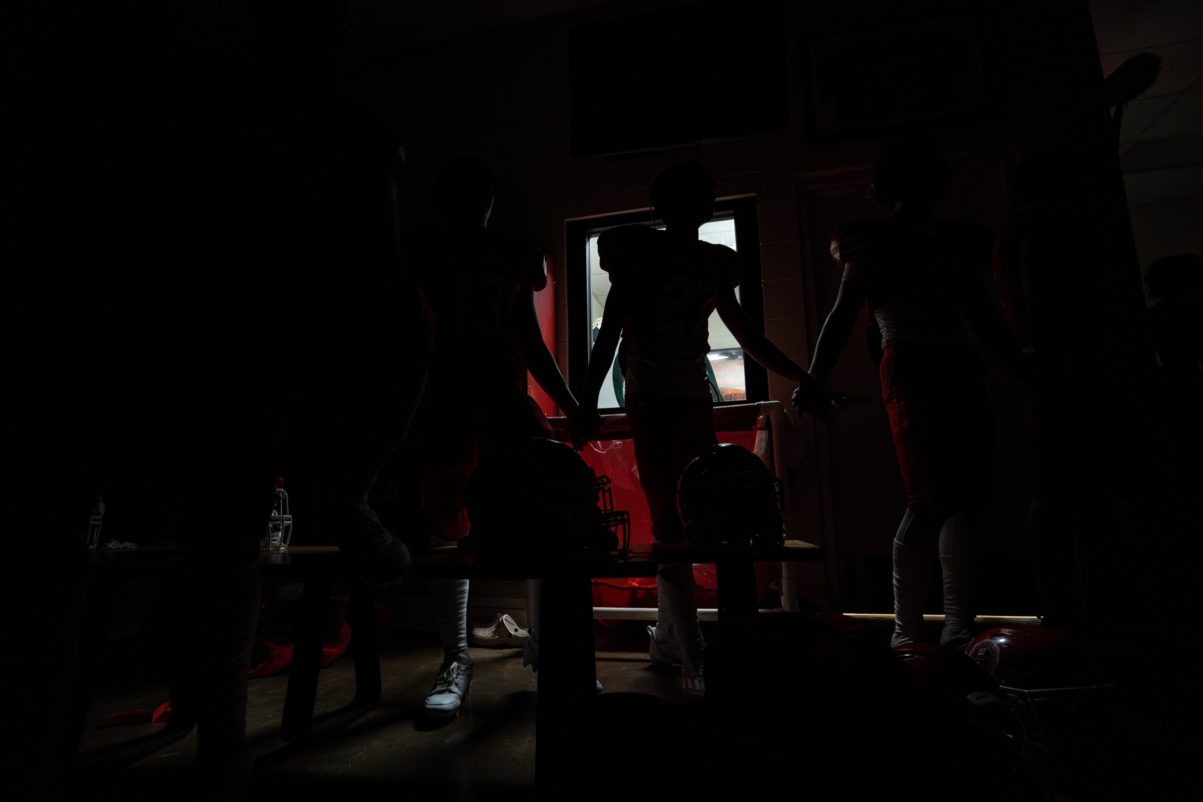 Lahainaluna football team hold their hands after the game in a darkened locker room and sing the alma mater in Hawaiian at Sue D. Cooley Stadium on Saturday, Oct. 21, 2023, in Lahaina, Hawaii. (AP Photo/Mengshin Lin)