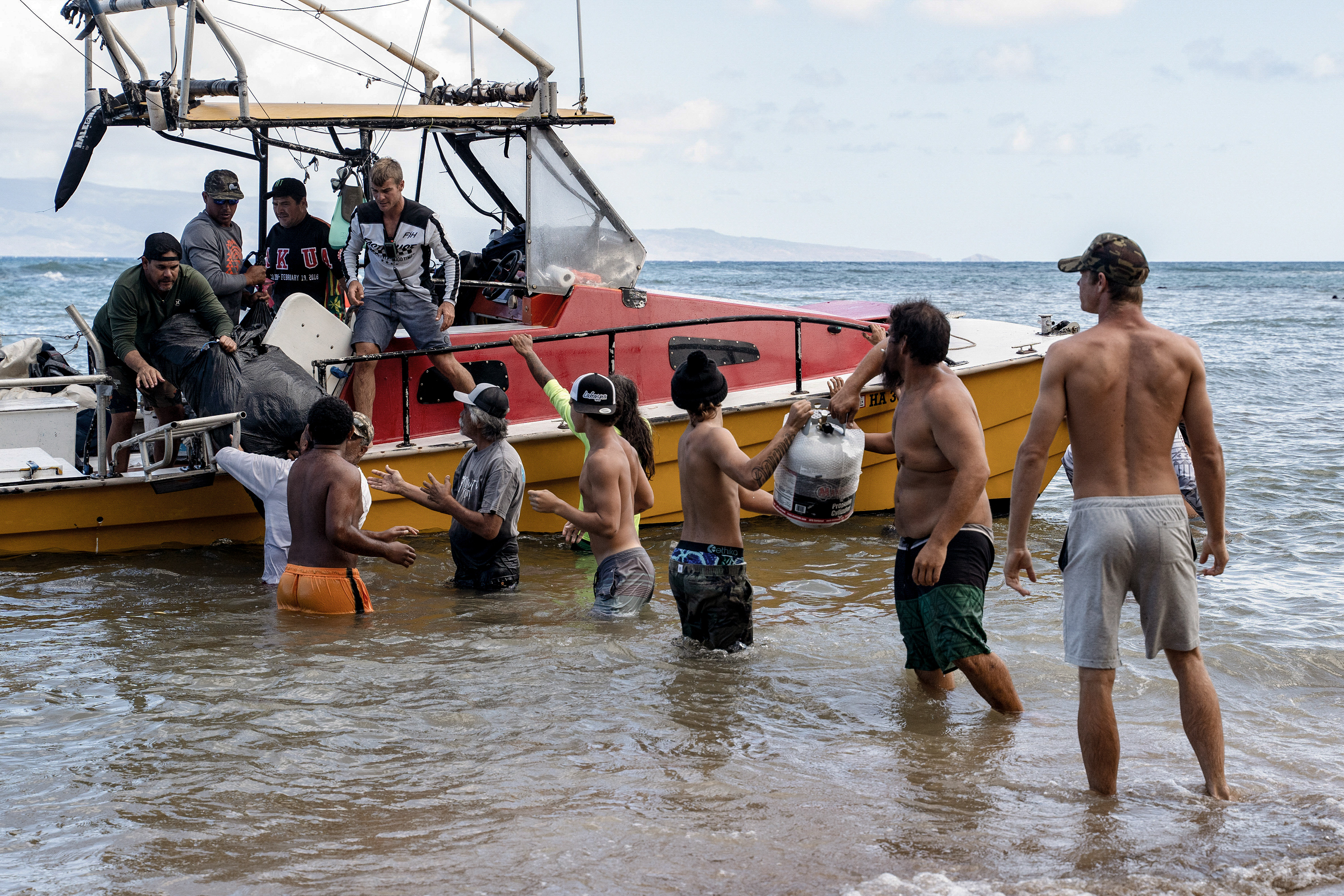 Kahana, HI - AUGUST 23: A boat loaded with supplies such as generators, gasoline, foods and other essentials, arrives in Kahana from Oahu in Kahana, Hawaii on August 10, 2023. Dozens of local residents of Kahana line up and step into the water to help pass down the supplies to shore. “The reason why we can stay positive is because how we seeing the community getting together” (Photo by Mengshin Lin for The Washington Post)