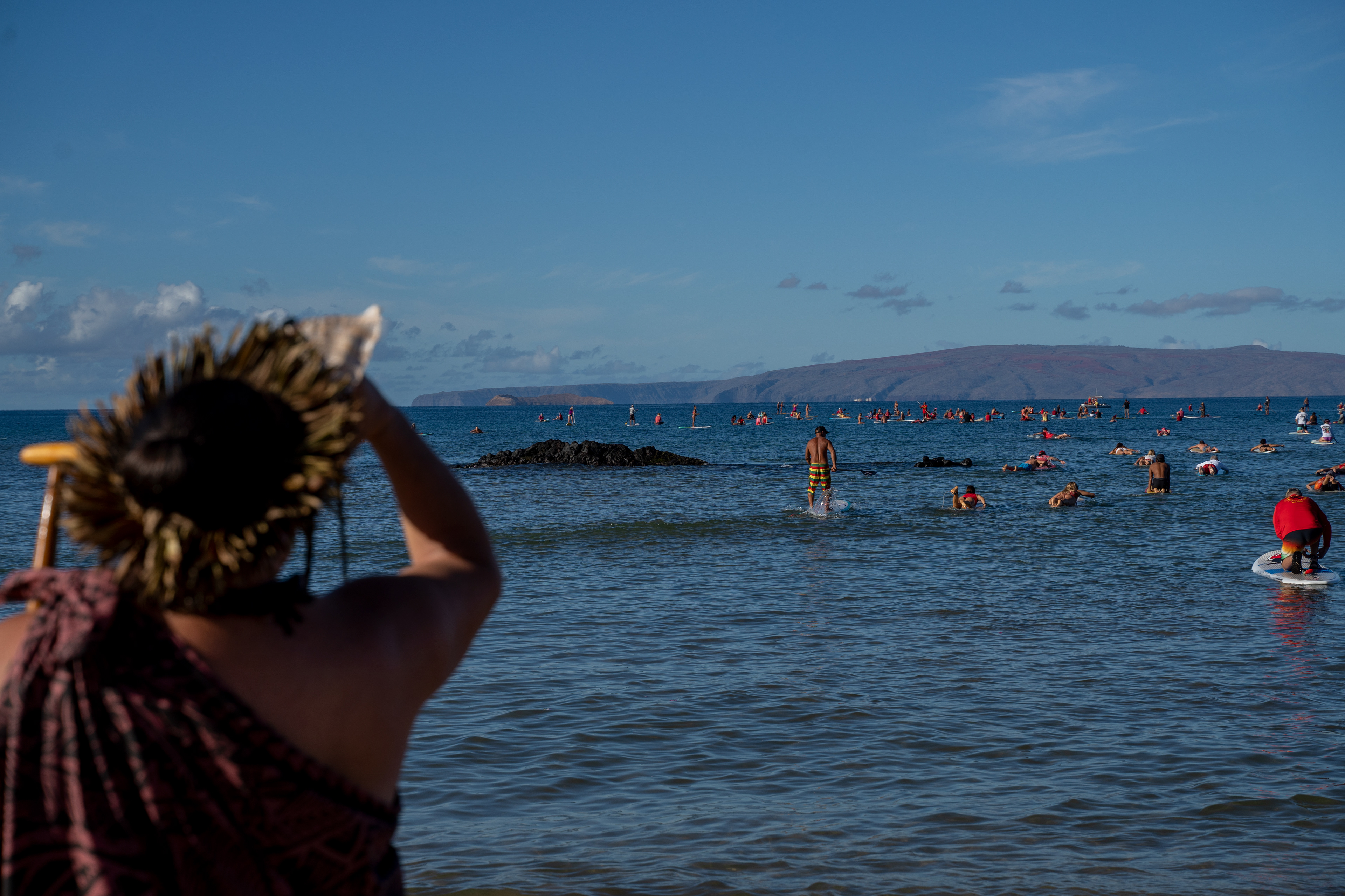 Kihei, HI - SEPTEMBER 8: Ua Aloha Maji, left, blows a pu (conch shell) as dozens surfers paddling out in memory of the Lahaina Fire at Kalama Beach Park in Kihei, Hawaii on September 8, 2023. (Photo by Mengshin Lin for The Washington Post)