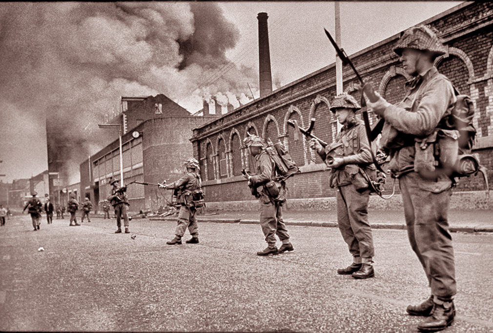 Falls Road, Belfast. Aug 15, 1969. Soldiers from The Regiment of Wales guard the burning Mercedes-Benz factory.