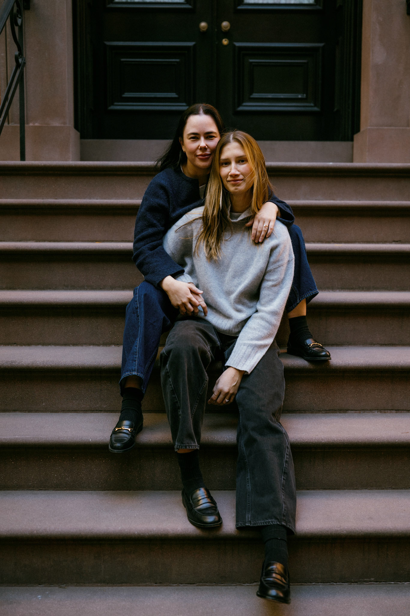 Lesbian couple sits on the stairs of a West Village brownstone.