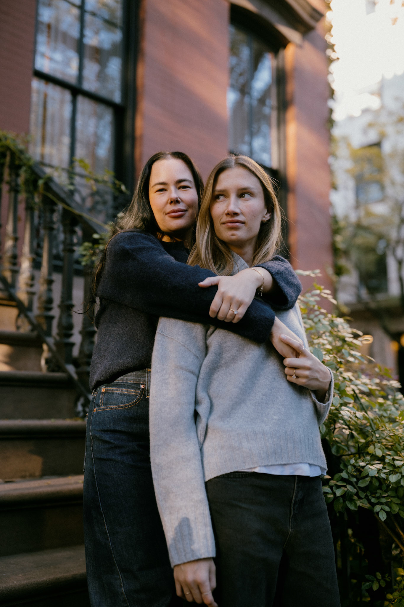 Woman holds other woman from behind in front of West Village brownstone