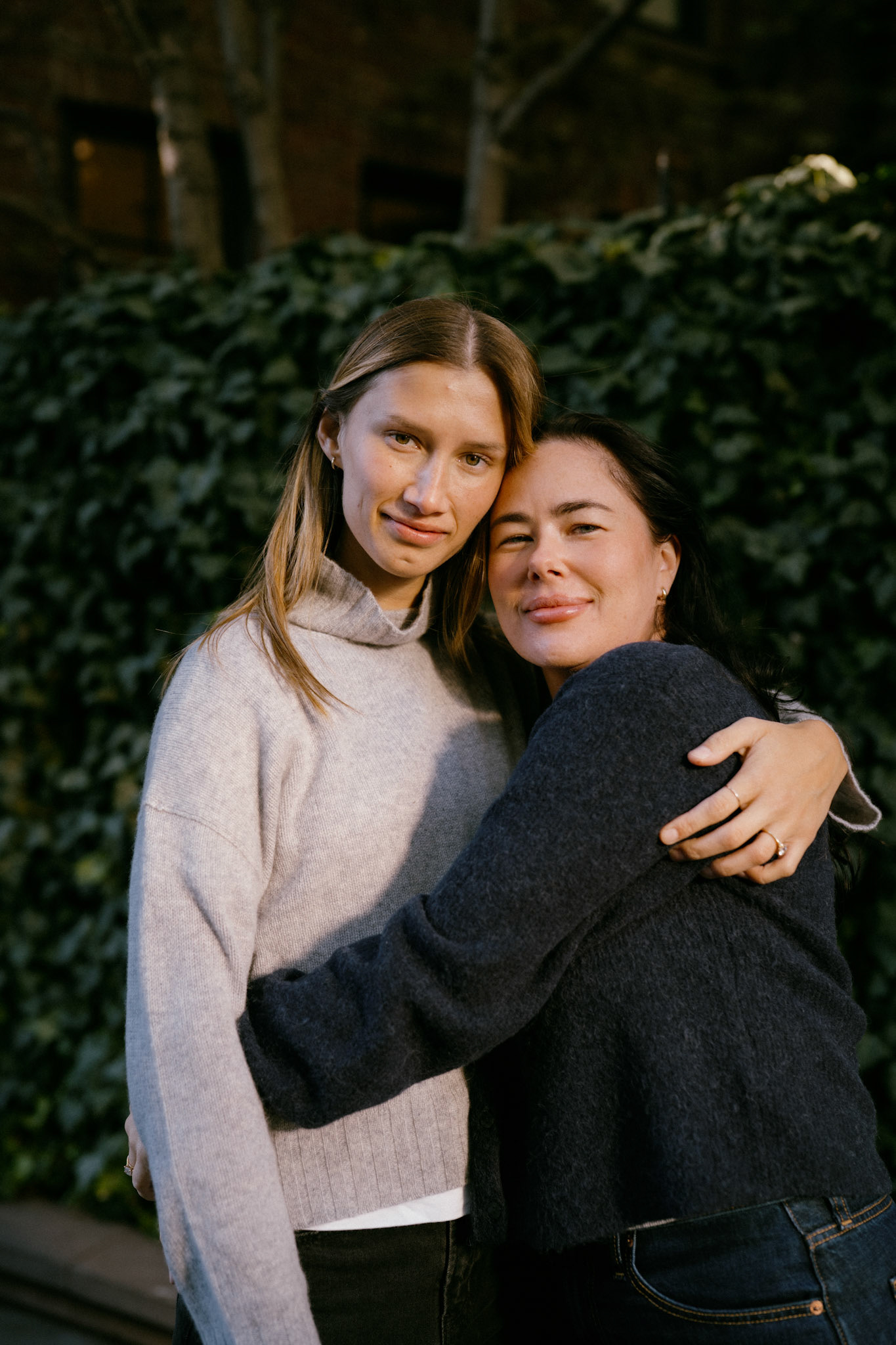 Lesbian couple embraces in front of West Village ivy.