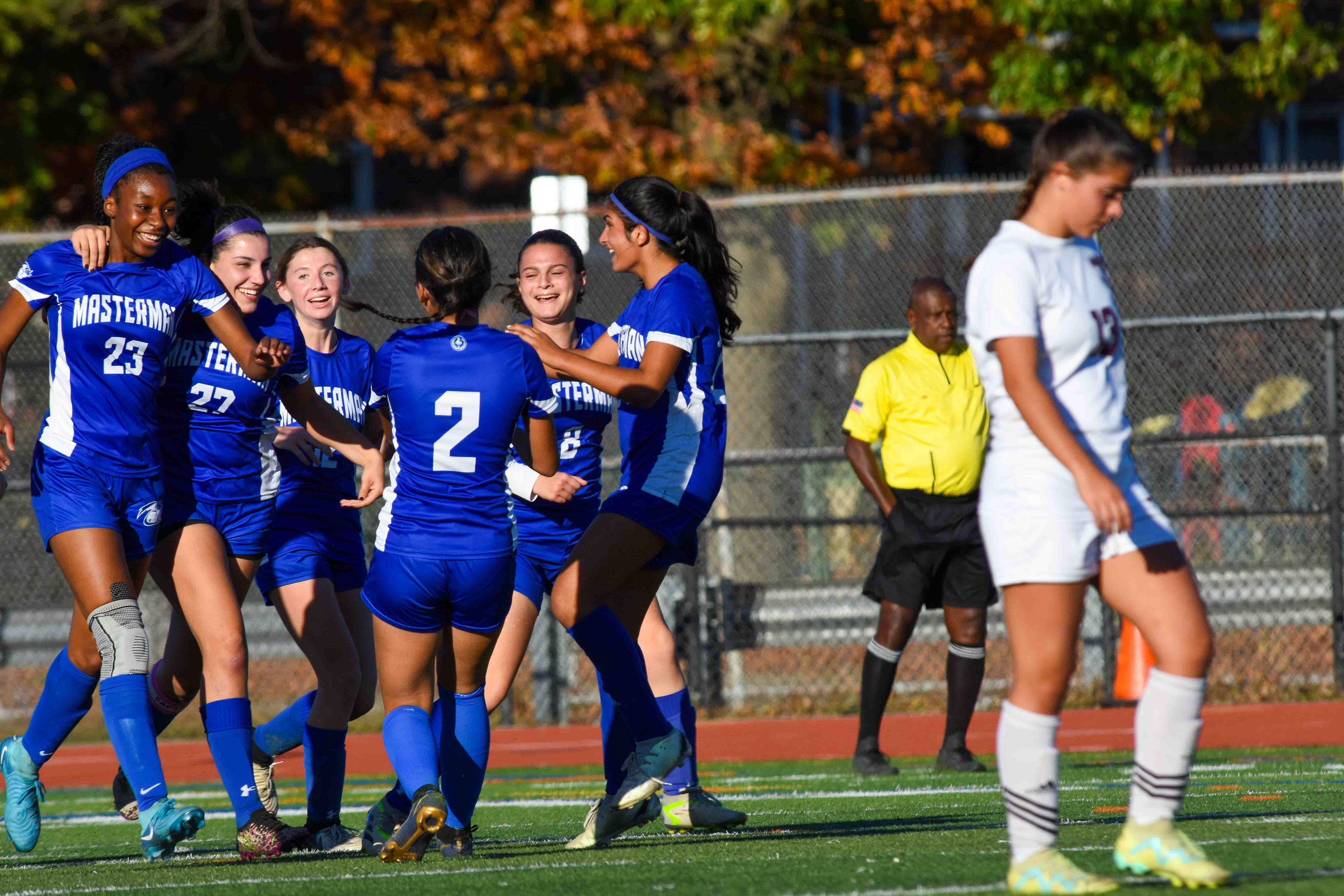 Great sports photography isn't just about the ball; it’s about the reaction. The photographer correctly identified that the story was happening after the goal, shifting focus to the huddle of celebrating players. This shot is a masterclass in storytelling through contrast. On the left, we see the bright blue huddle of joy; on the right, the white-shirted opponent walks away in dejection. It captures the dual nature of competition in one frame.